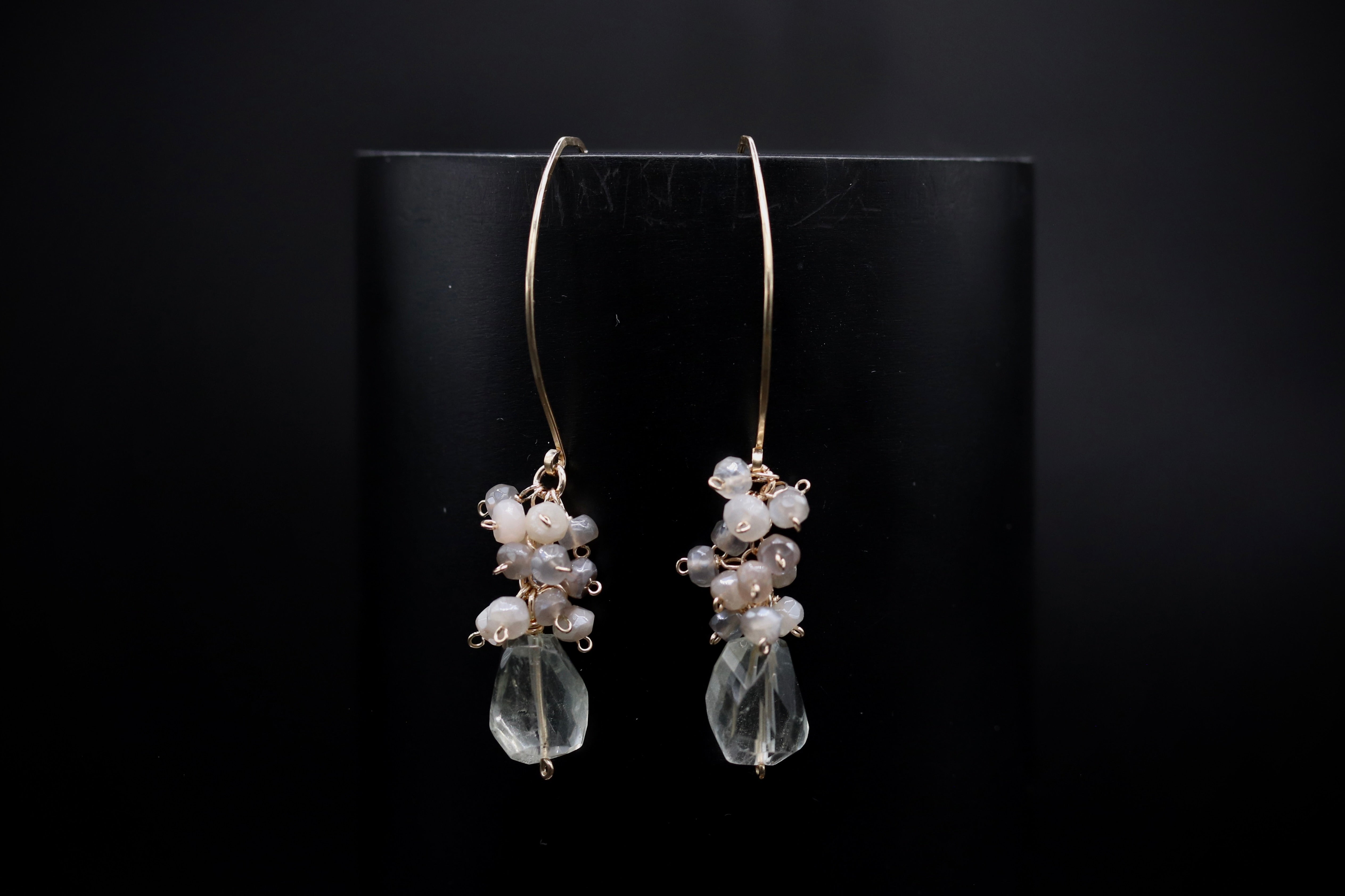 A pair of elegant earrings with clear gemstone accents and pearl-like stones, displayed against a dark background.