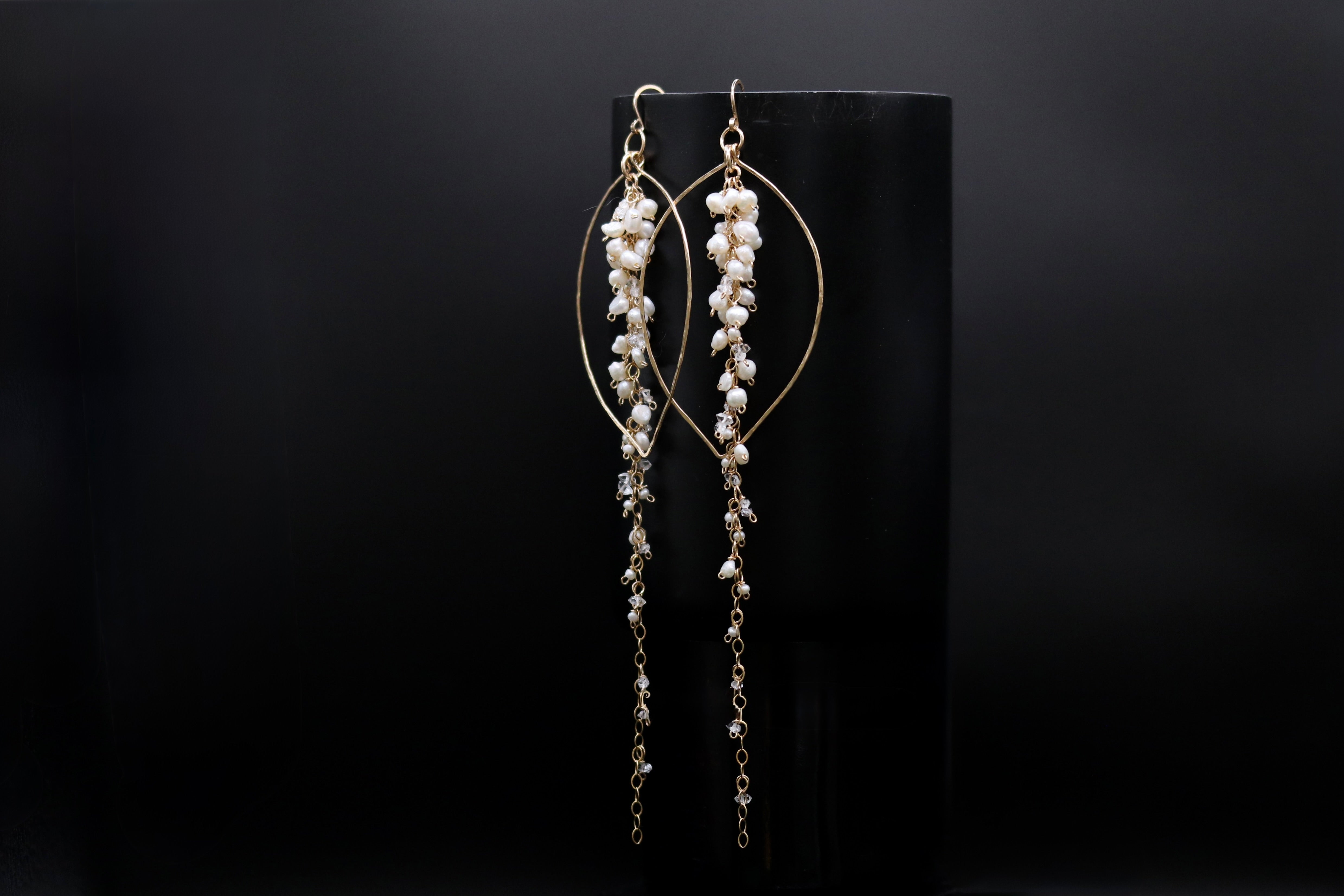A pair of elegant gold earrings with dangling pearls against a dark background.