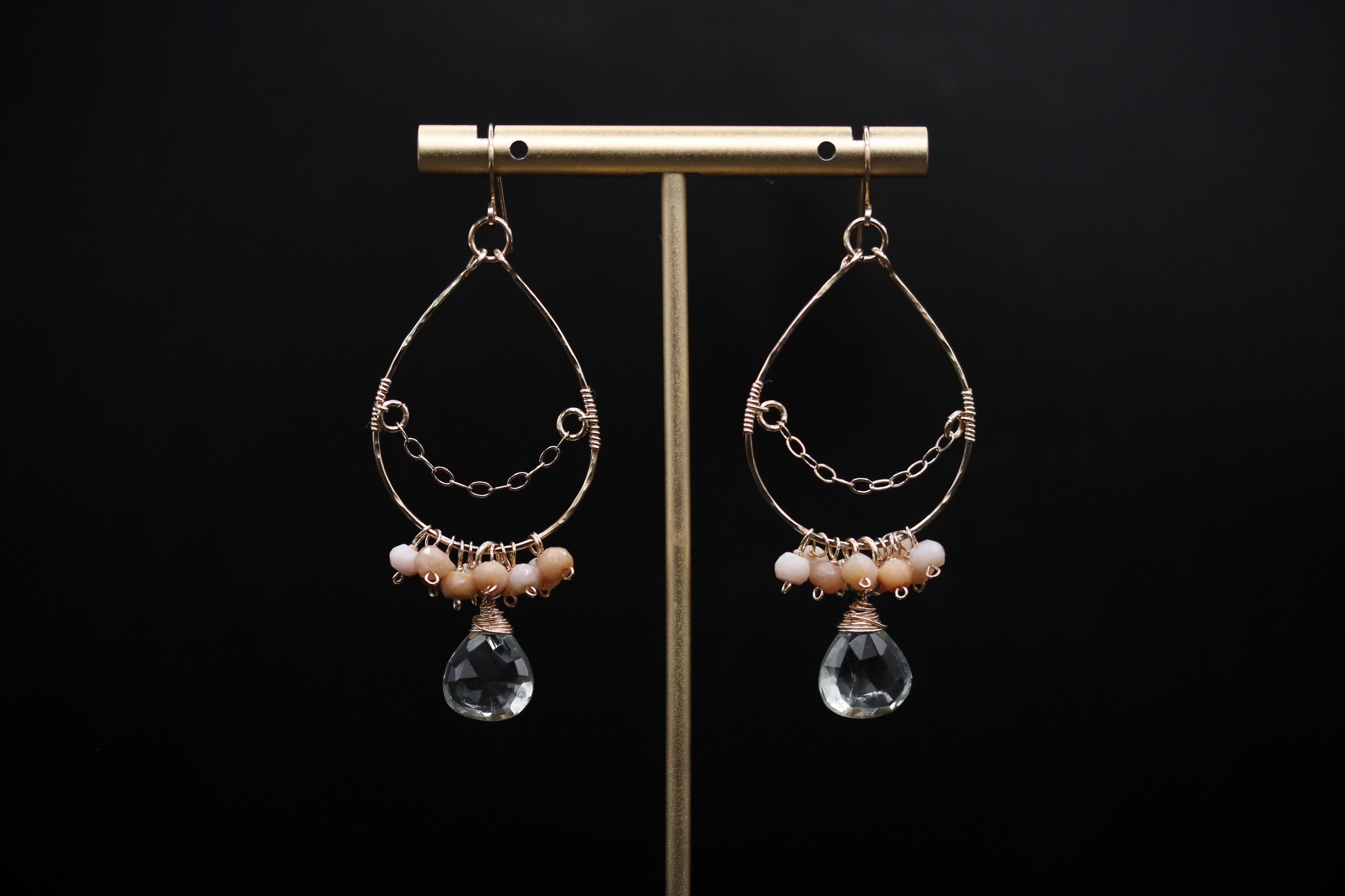 A pair of elegant earrings with clear gemstone accents and metal wirework, displayed on a gold stand against a black background.