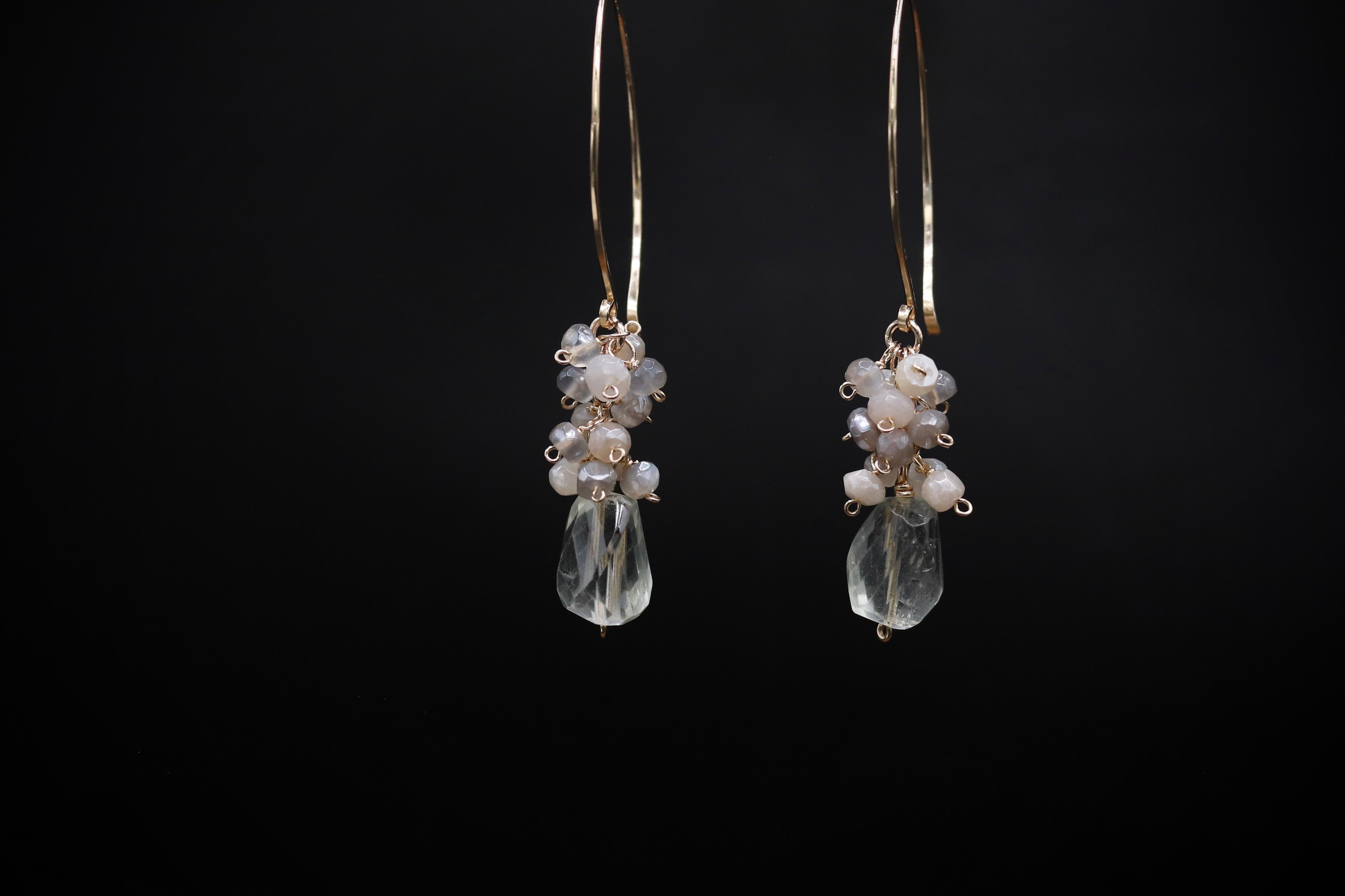 A pair of elegant earrings with clear beads and metal hooks against a black background.