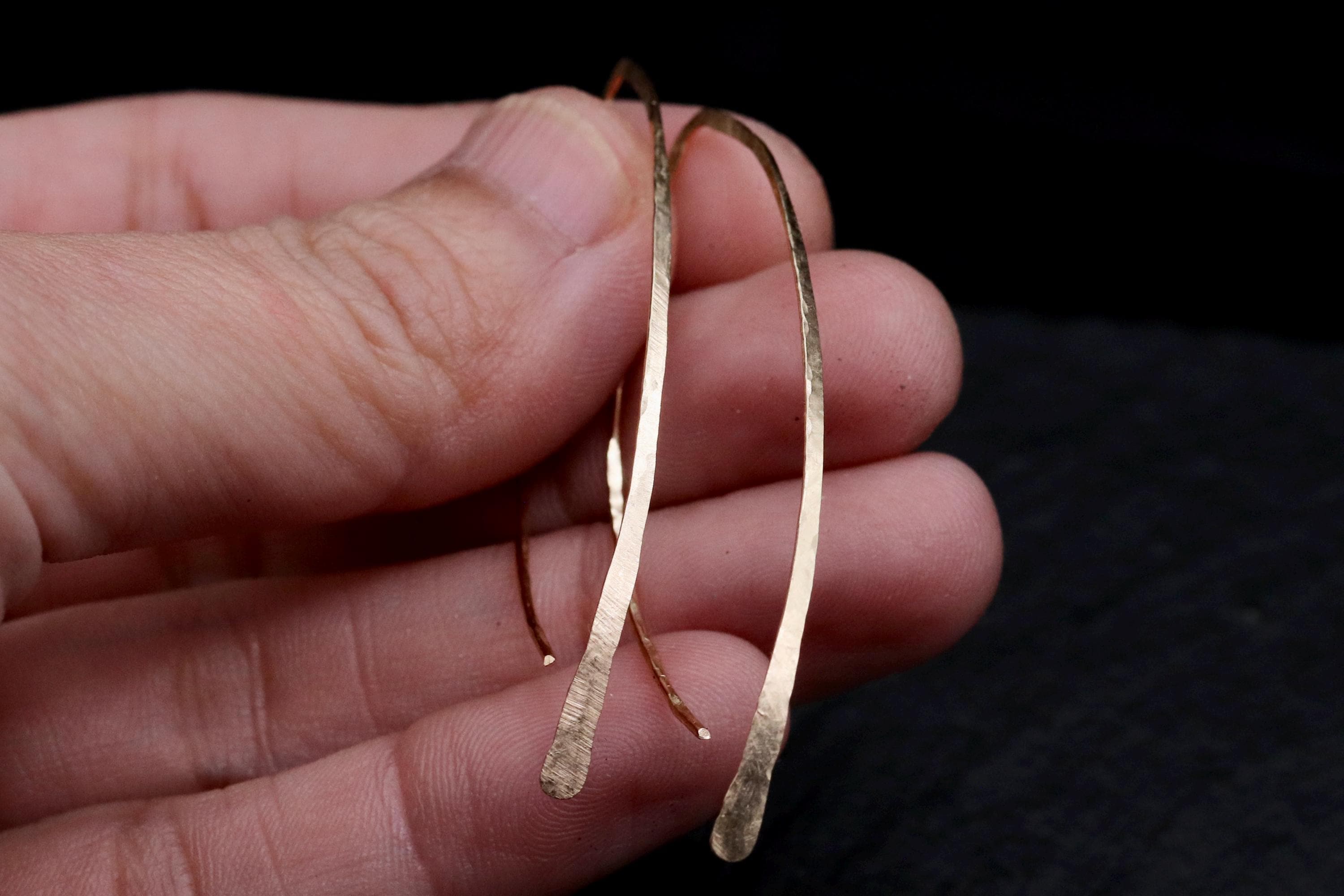 A hand holding a pair of gold-colored earrings against a dark background.