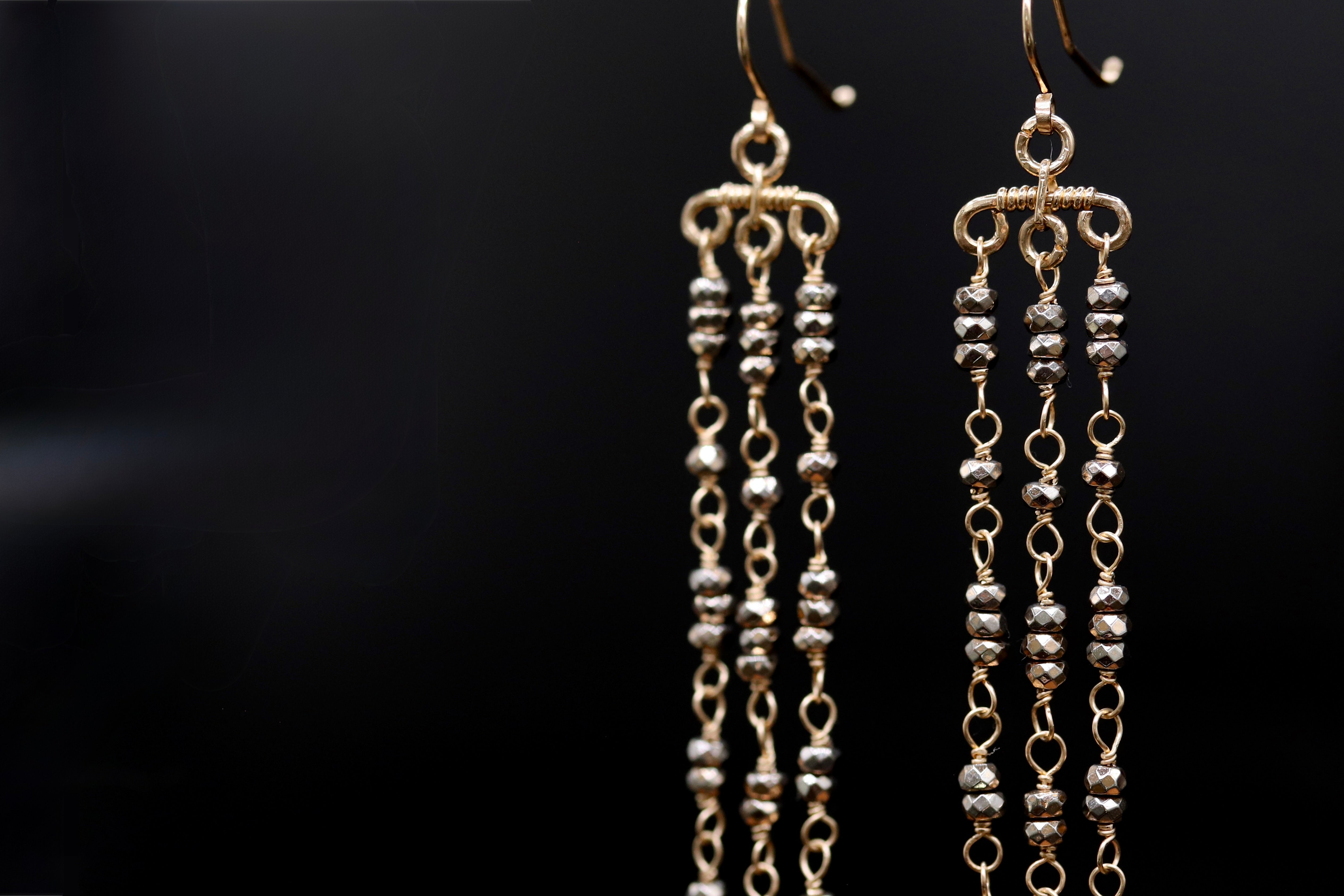 A pair of gold earrings with multiple tiers of small, dangling beads against a black background.