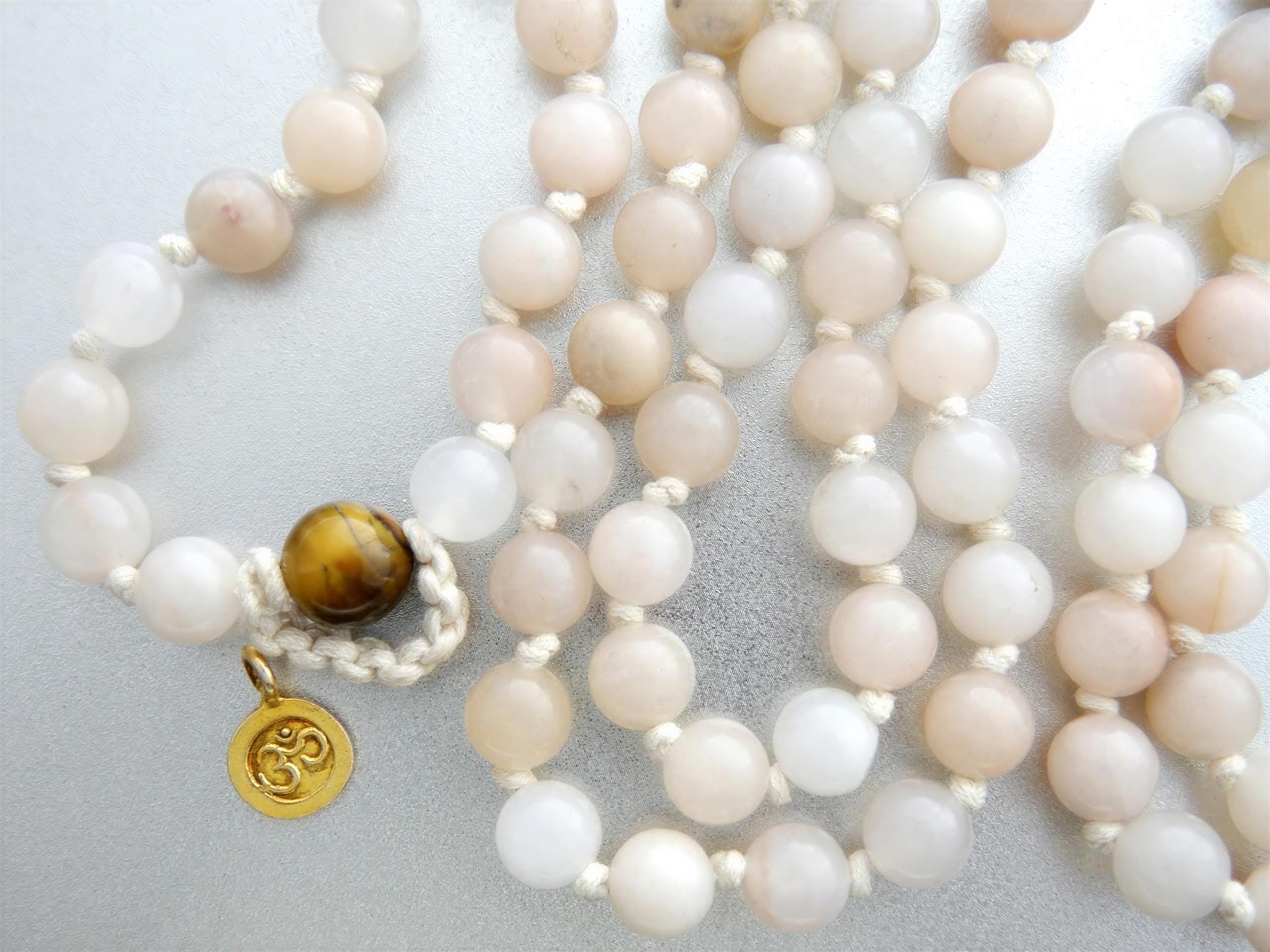 A beaded necklace with a gold pendant, featuring a circular design with a symbol on it, resting on a white surface.