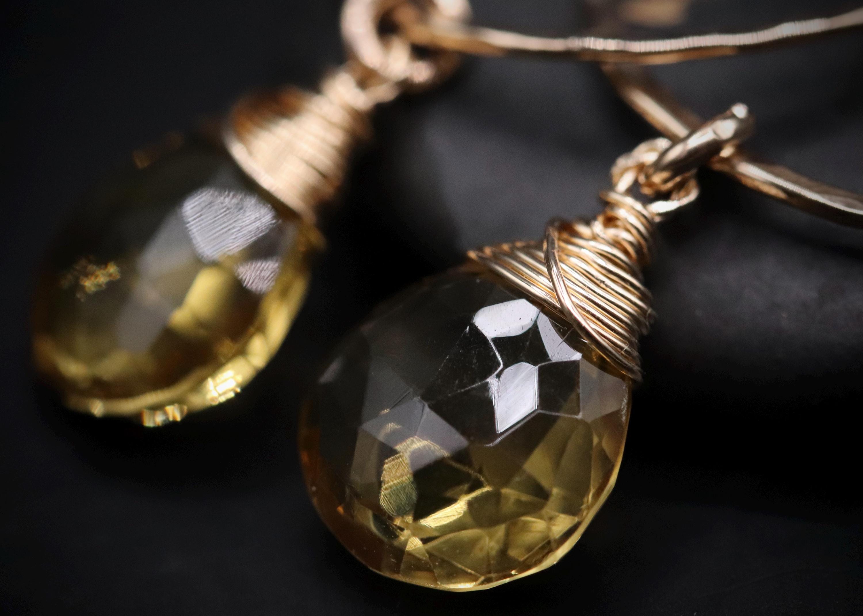 A close-up image of a pair of gold-colored earrings with clear gemstone pendants.
