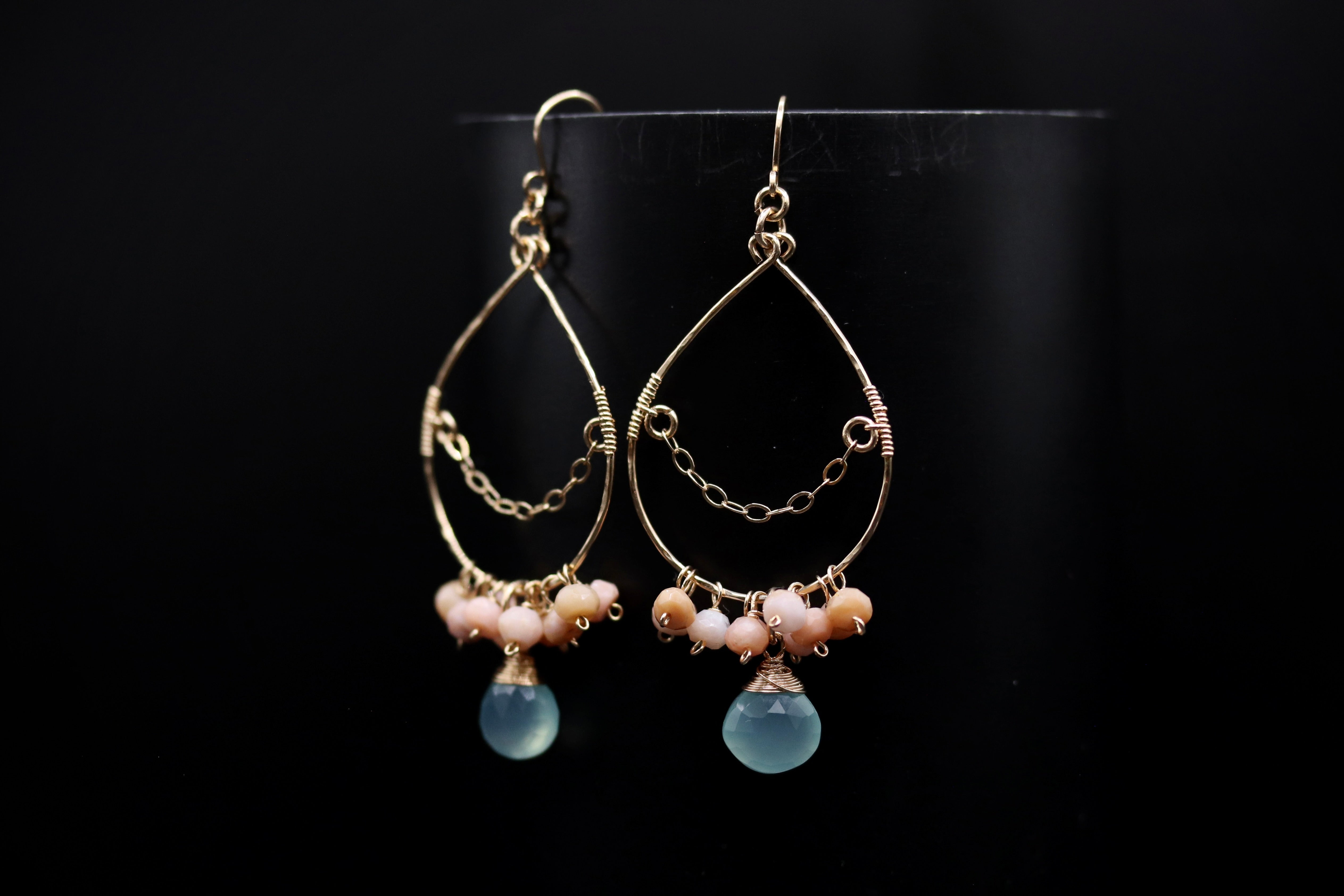 A pair of gold earrings with blue and pink stones hanging from them against a black background.