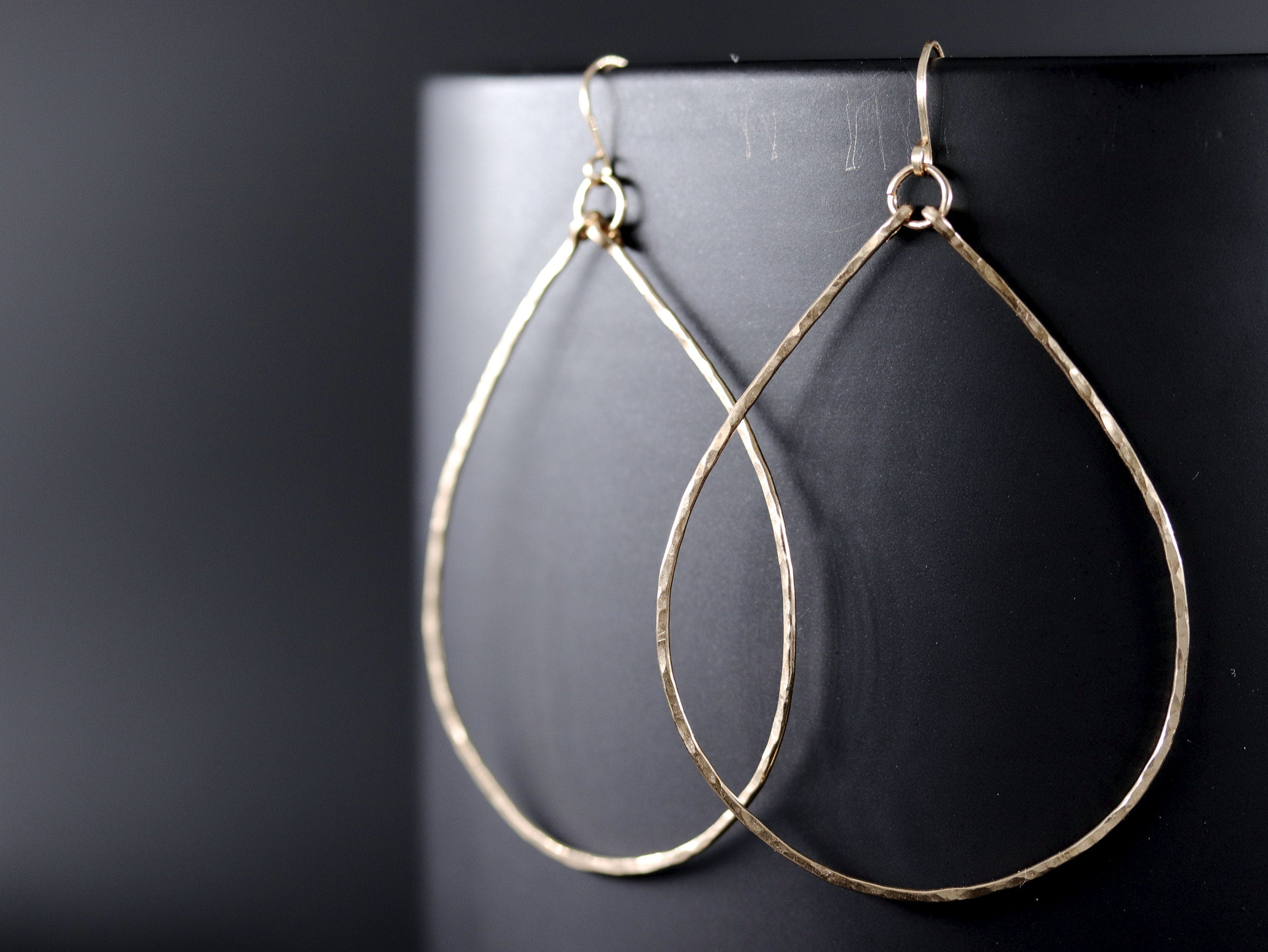 May include: A pair of gold teardrop-shaped hoop earrings. The earrings are made of hammered metal and have a delicate, organic look.