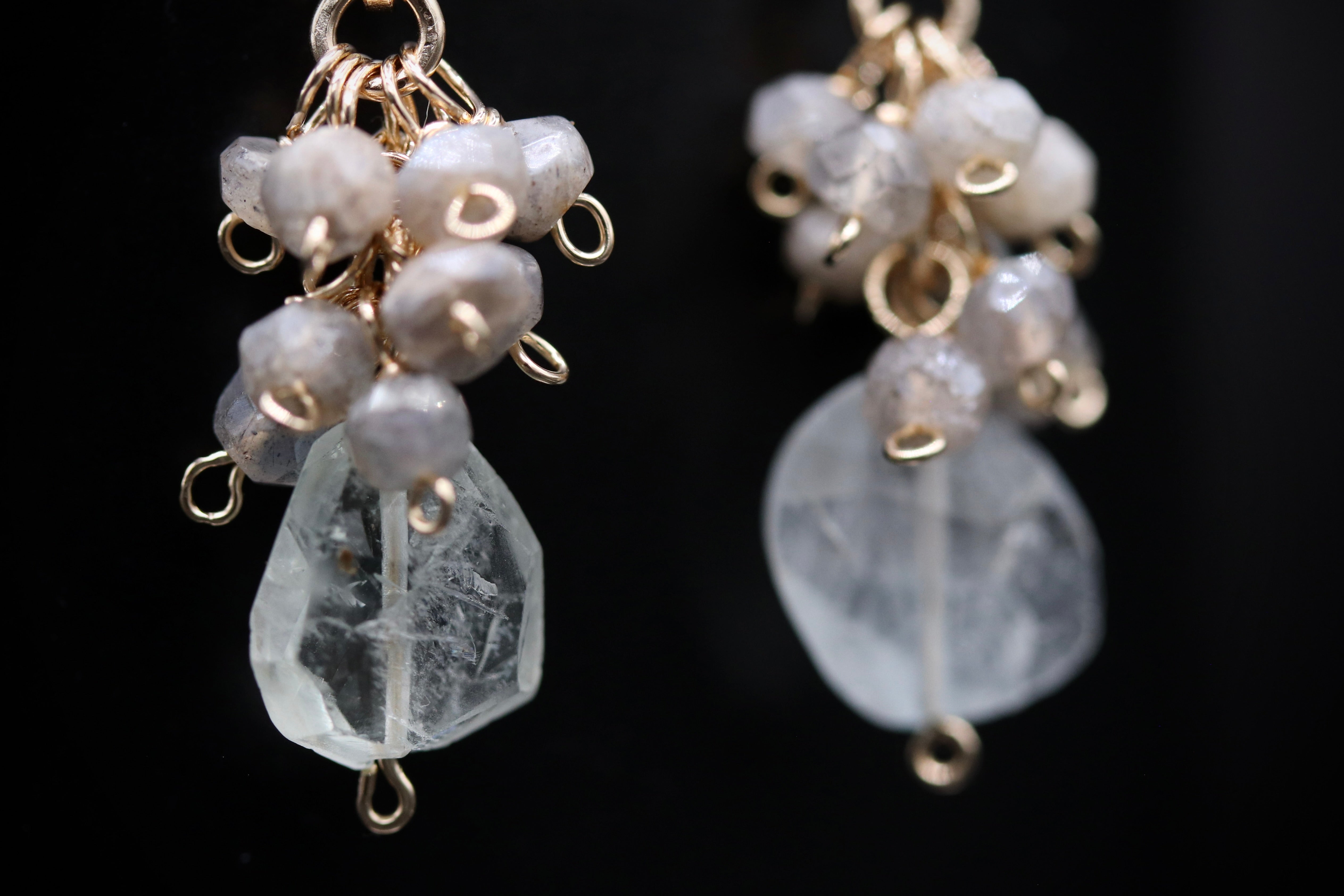 A close-up view of a pair of earrings with clear gemstone-like stones and metal hooks.