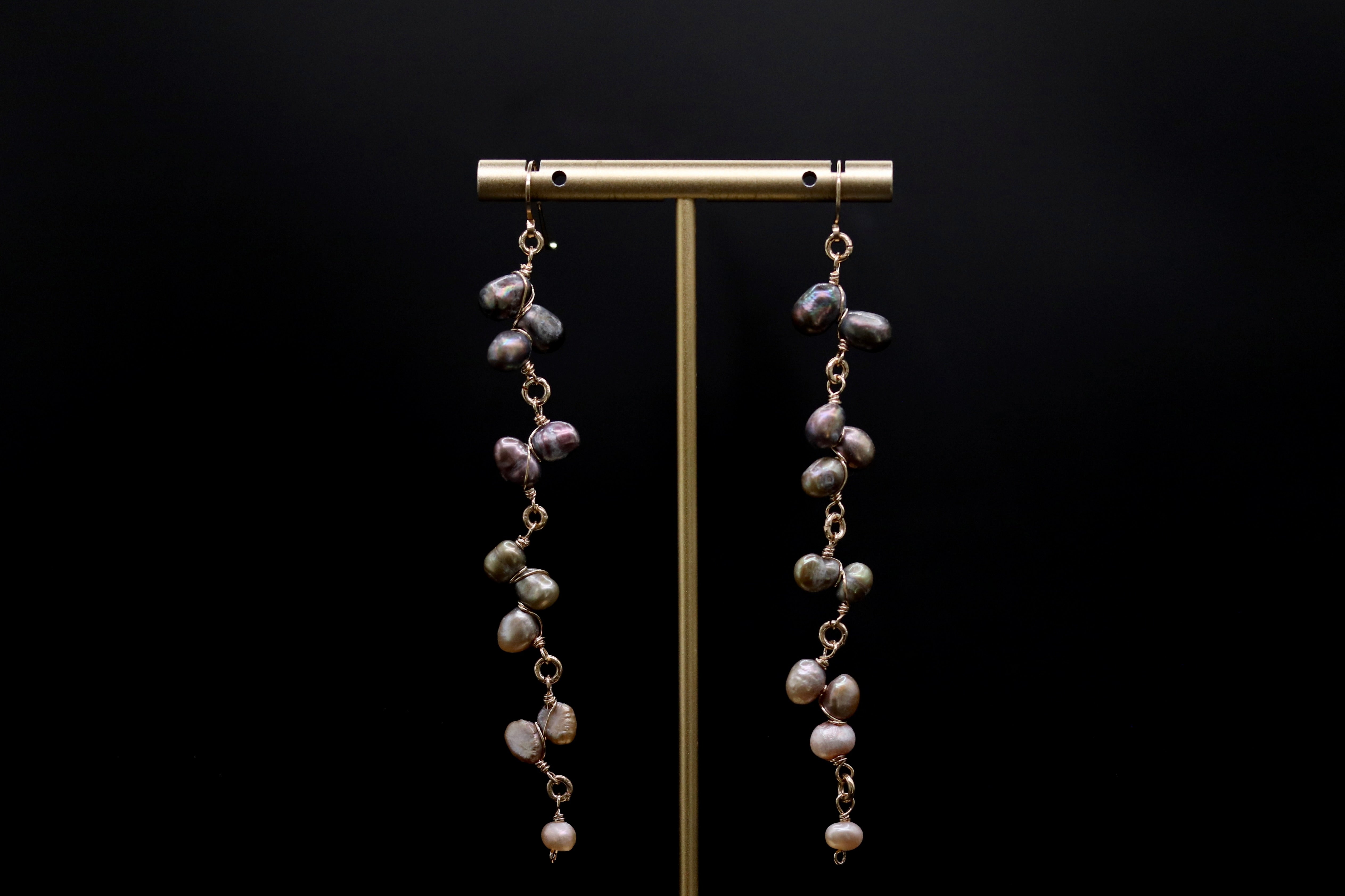A pair of earrings with multiple strands of pearls hanging from a gold stand against a black background.