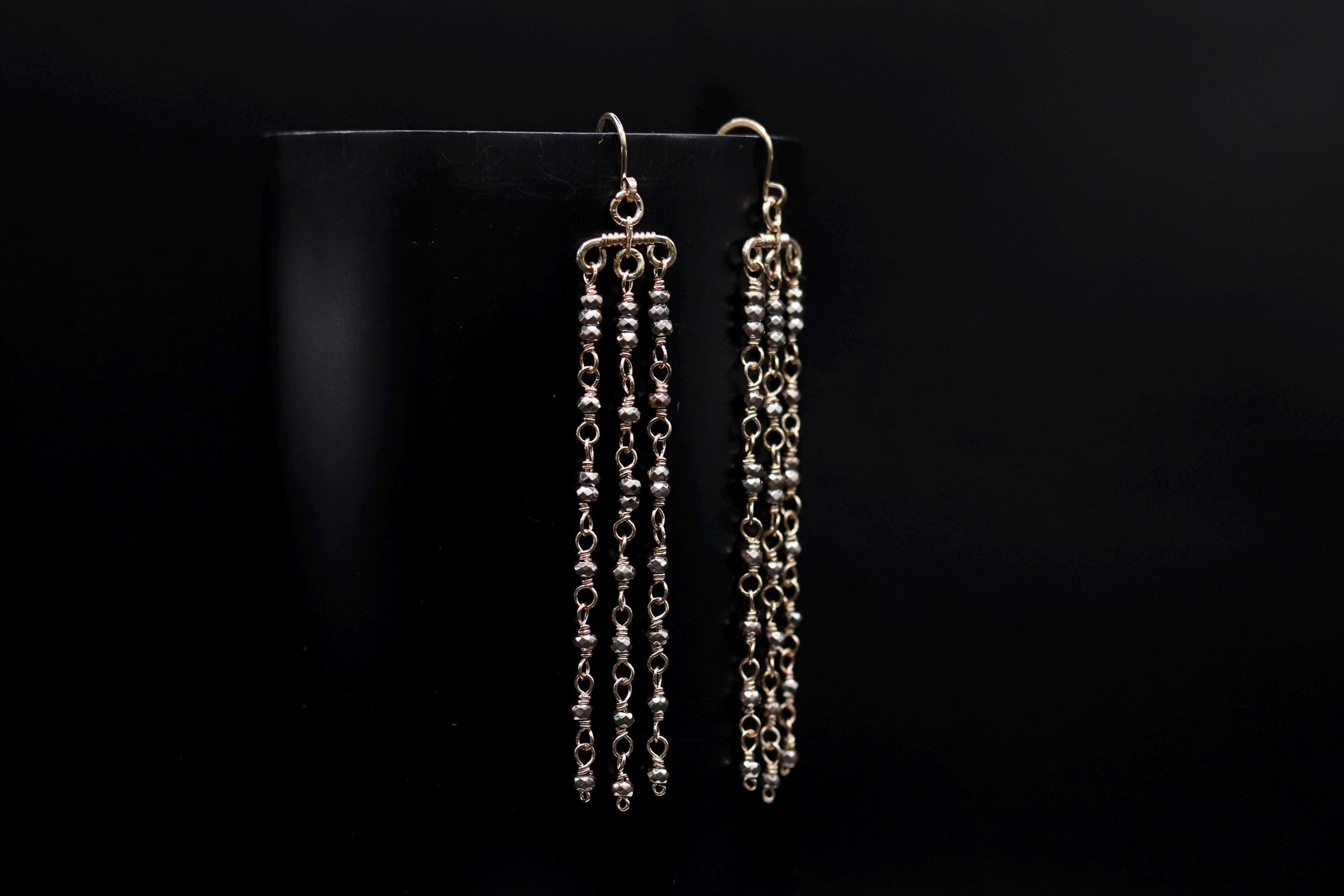 A pair of gold earrings with long, dangling chains against a black background.