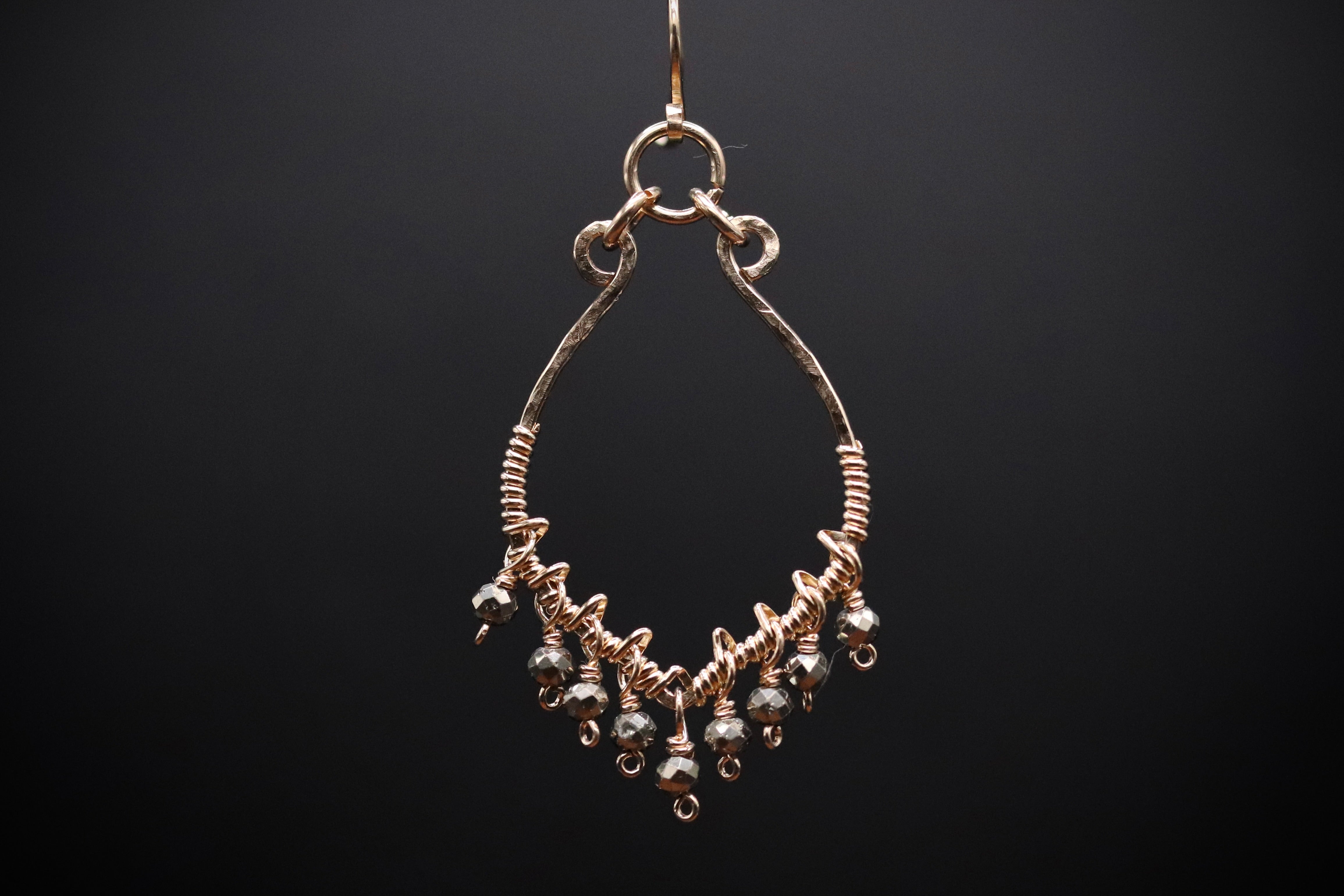A gold-colored earring with a twisted design and dangling beads is shown against a dark background.