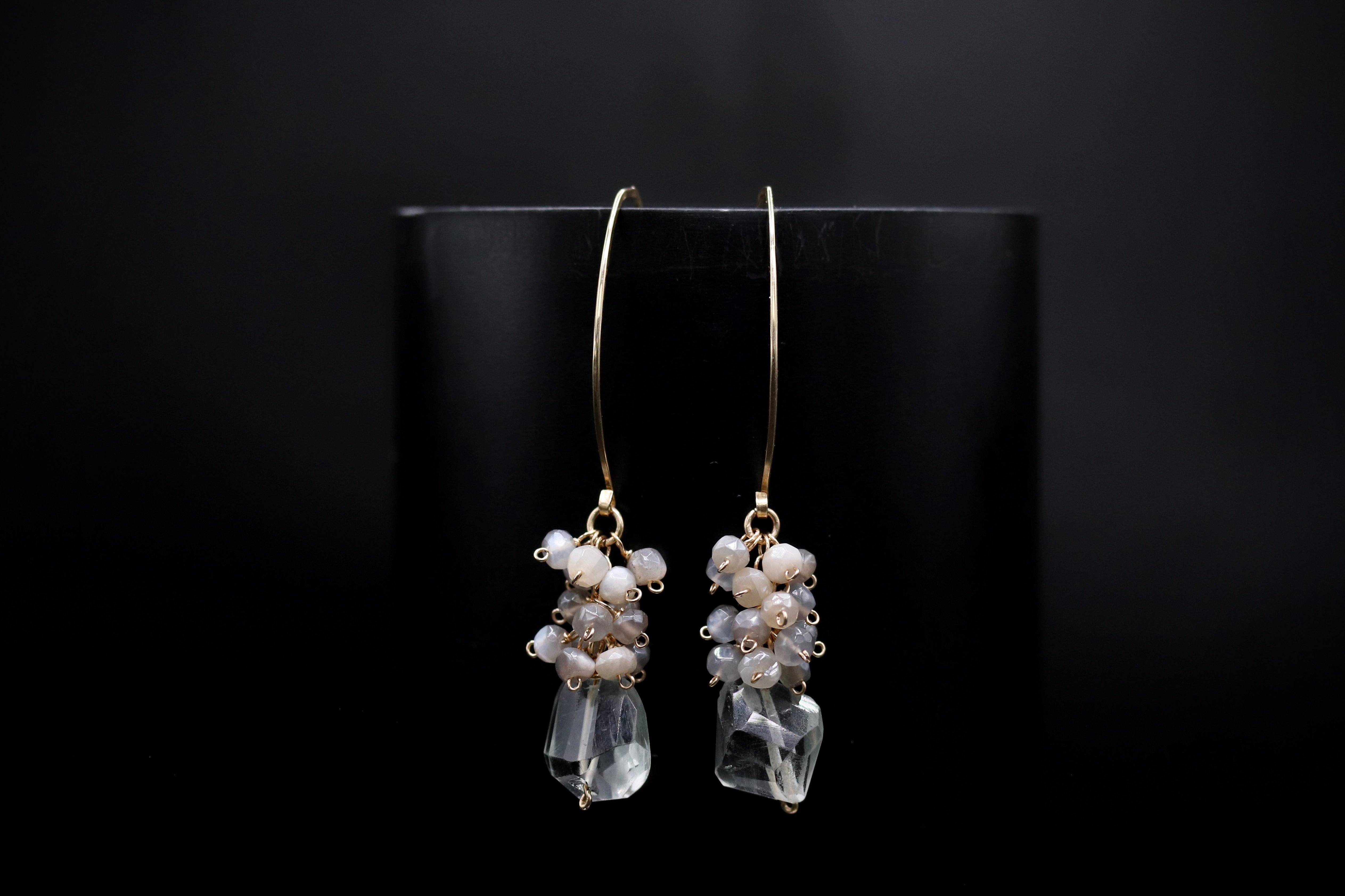 A pair of elegant earrings with clear gemstone accents and dangling gold hooks, displayed against a dark background.