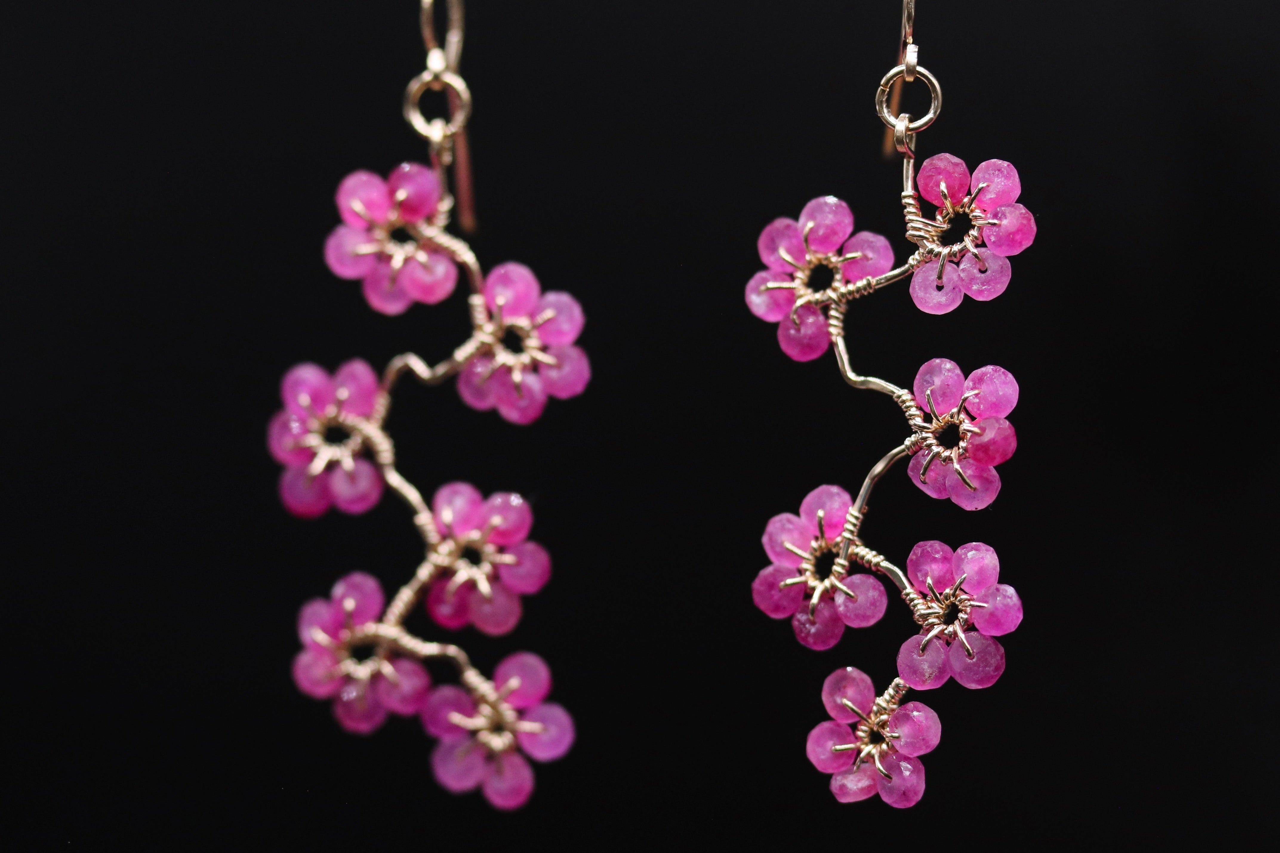 A pair of delicate earrings with small, pink flower-shaped charms hanging from a wire.