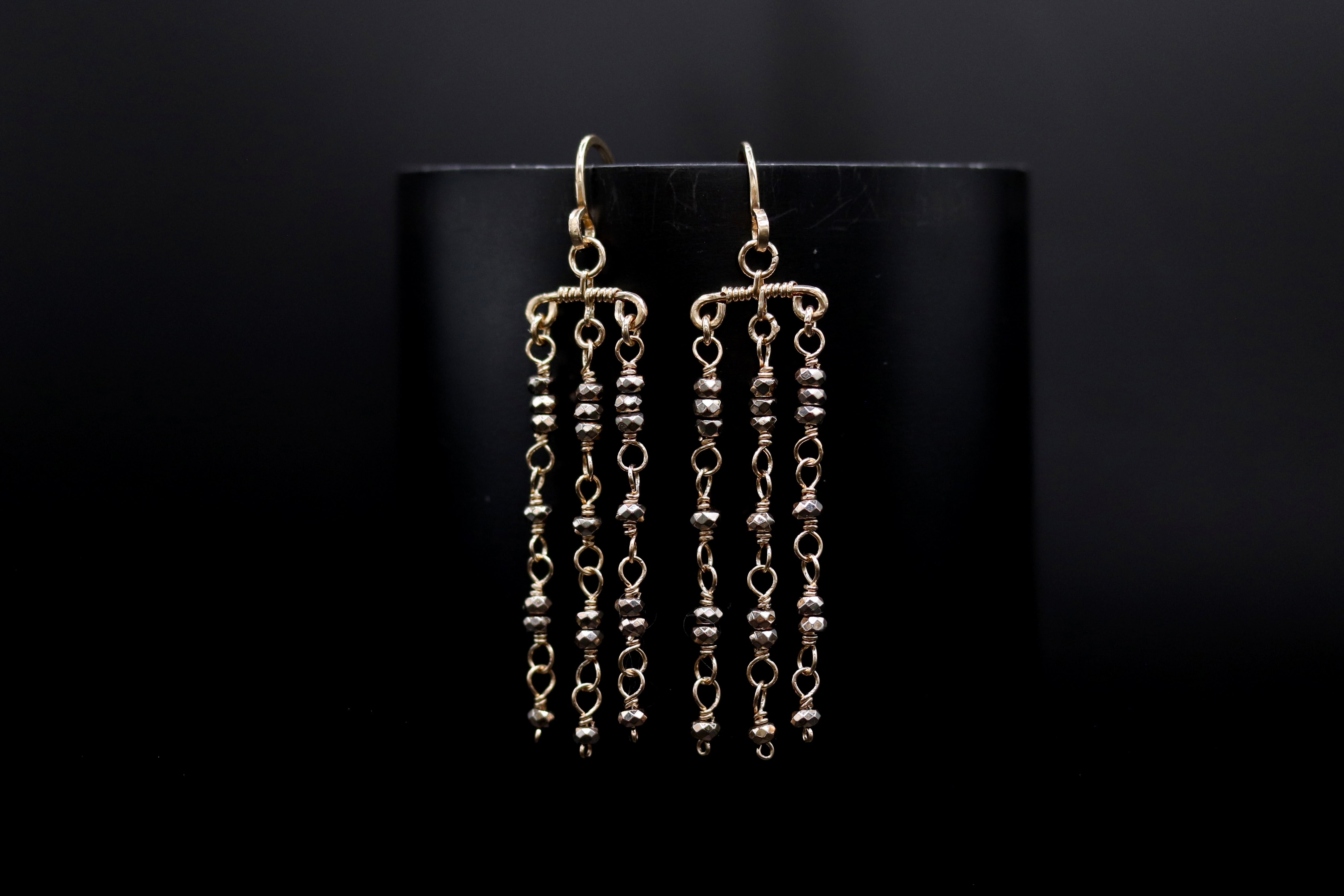 A pair of gold earrings with dangling chains and beads against a black background.