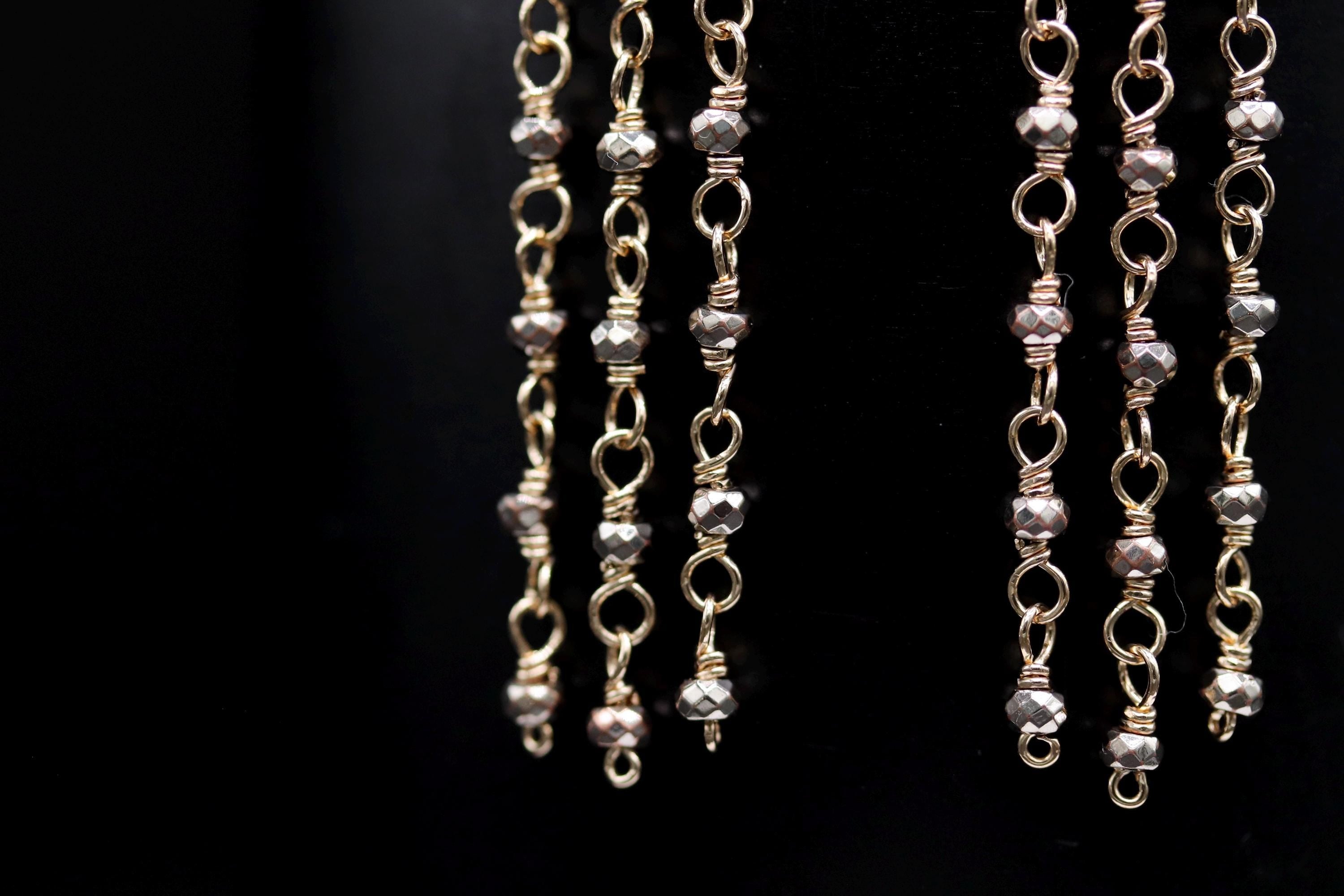 A close-up view of a collection of gold-colored metal chains with small, round beads hanging from them, creating a visually striking and intricate design.