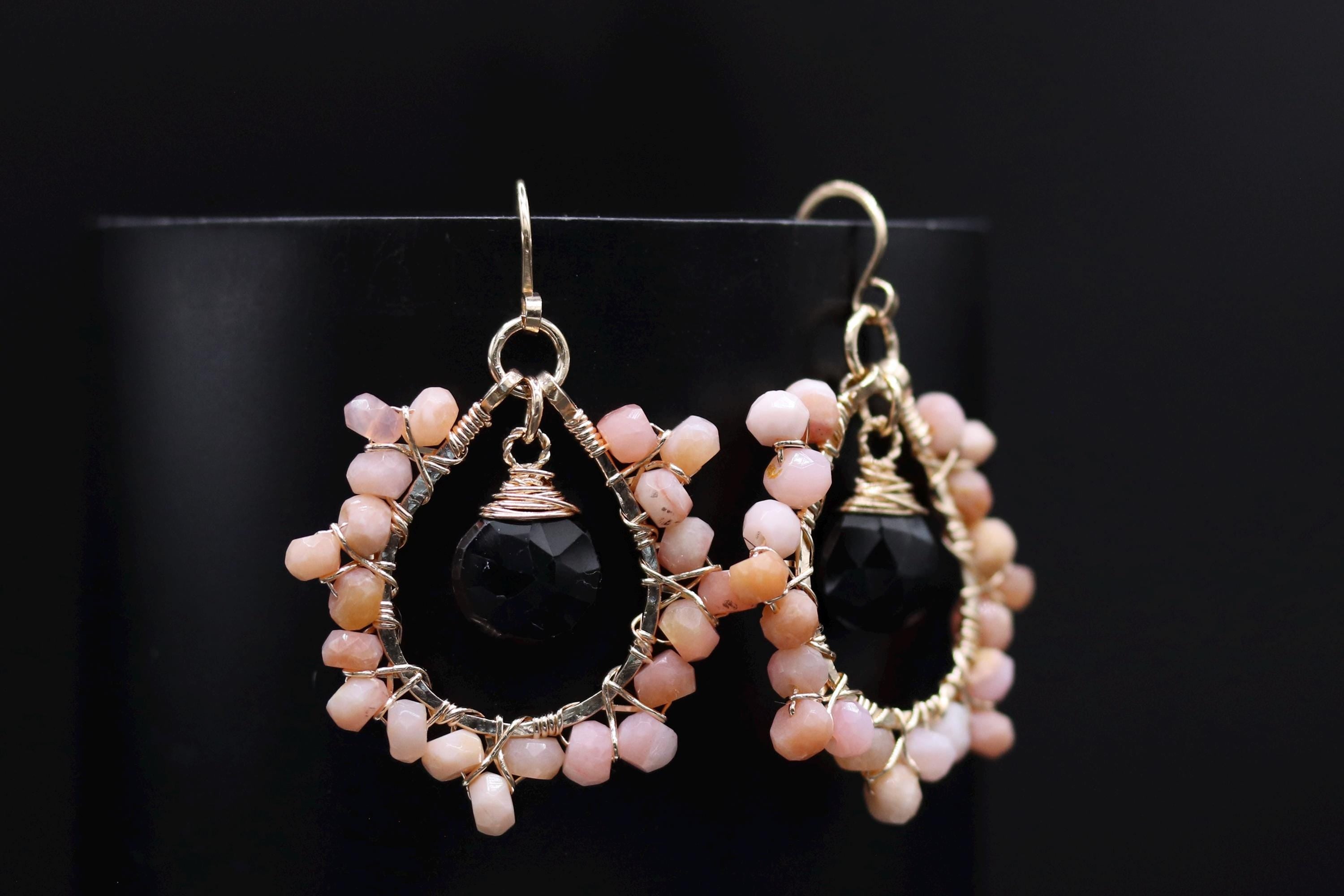 A pair of elegant earrings with a black stone and beige stone bead design, set against a black background.