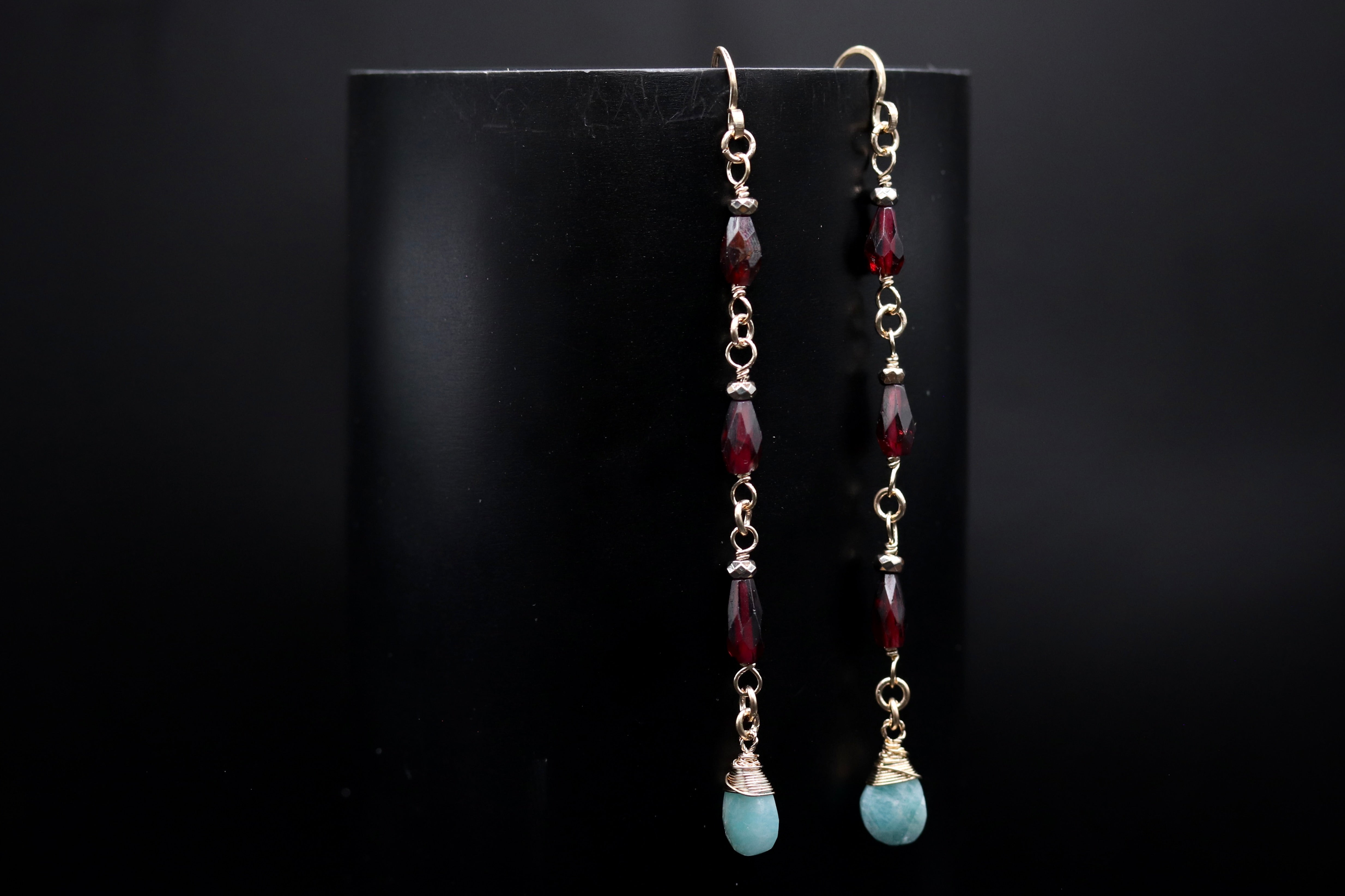 A pair of earrings with red and blue gemstones hanging from the bottom, displayed against a black background.