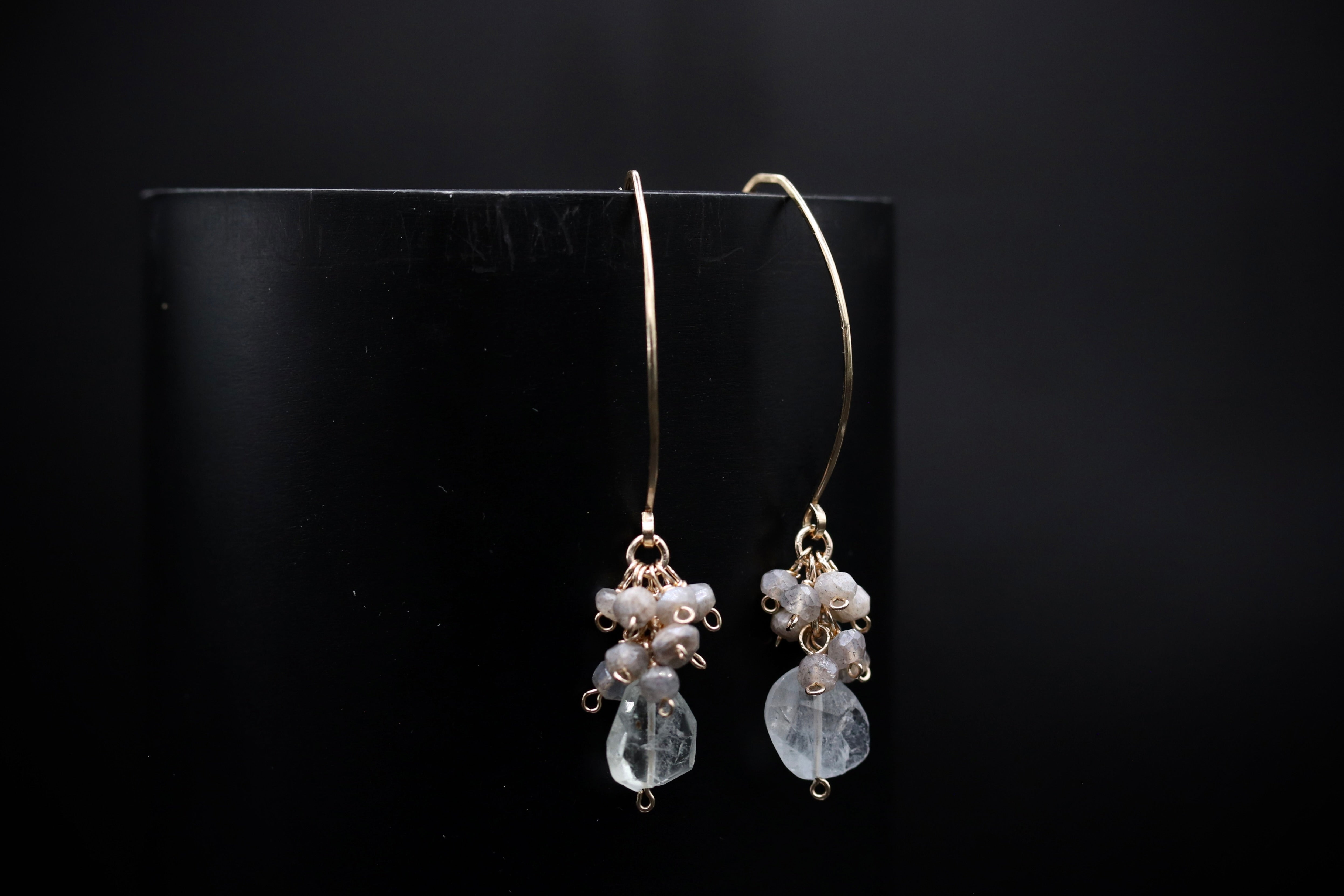 A pair of elegant earrings with clear stones and metal hooks, displayed against a black background.