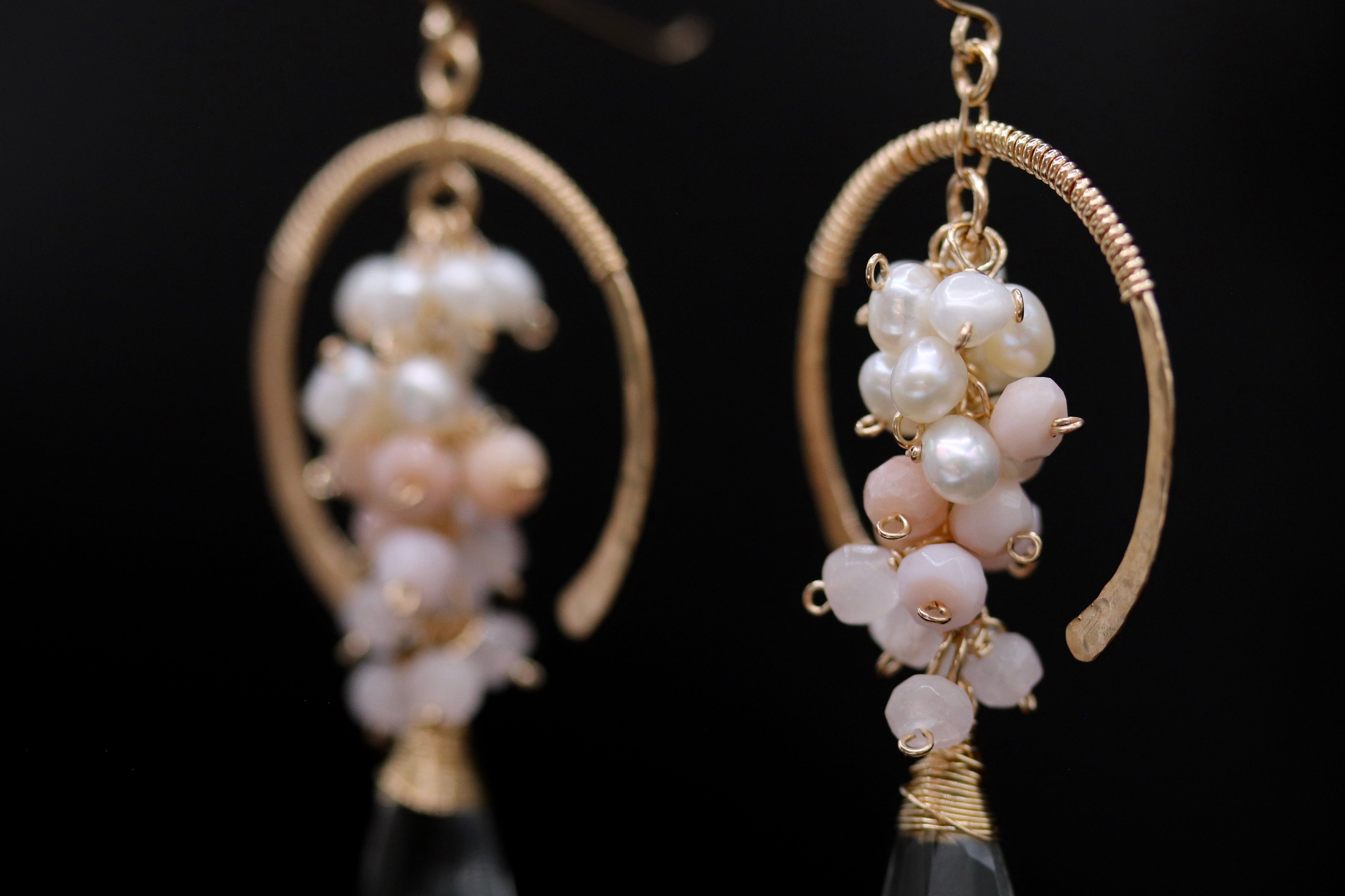 A pair of elegant earrings with a combination of white and pink pearls, as well as small white and pink beads, hanging from a gold-colored metal frame.