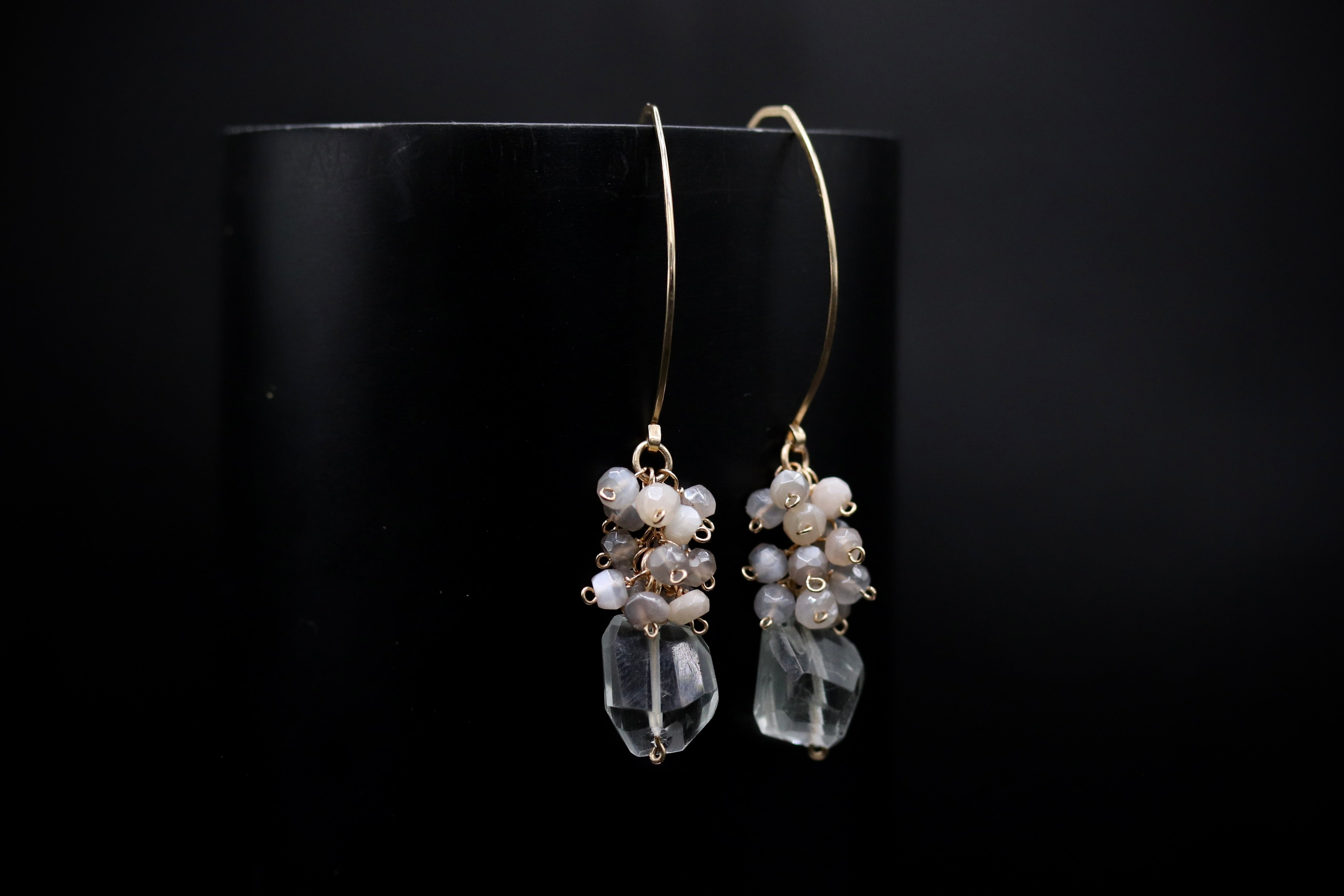 A pair of elegant earrings with clear gemstone accents and dangling from a gold hook against a black background.