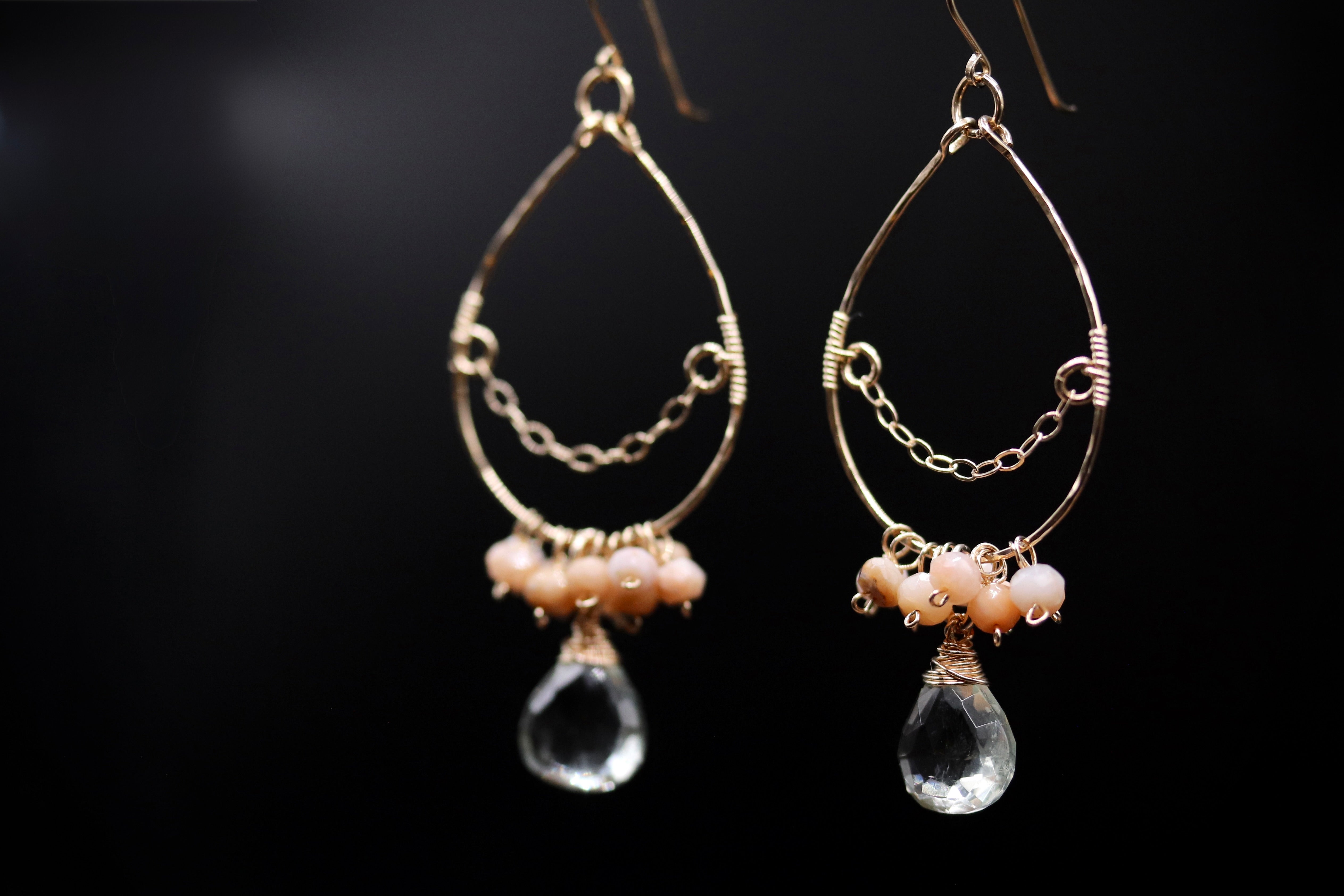 A pair of elegant earrings with a clear crystal pendant and small beads hanging from the bottom.