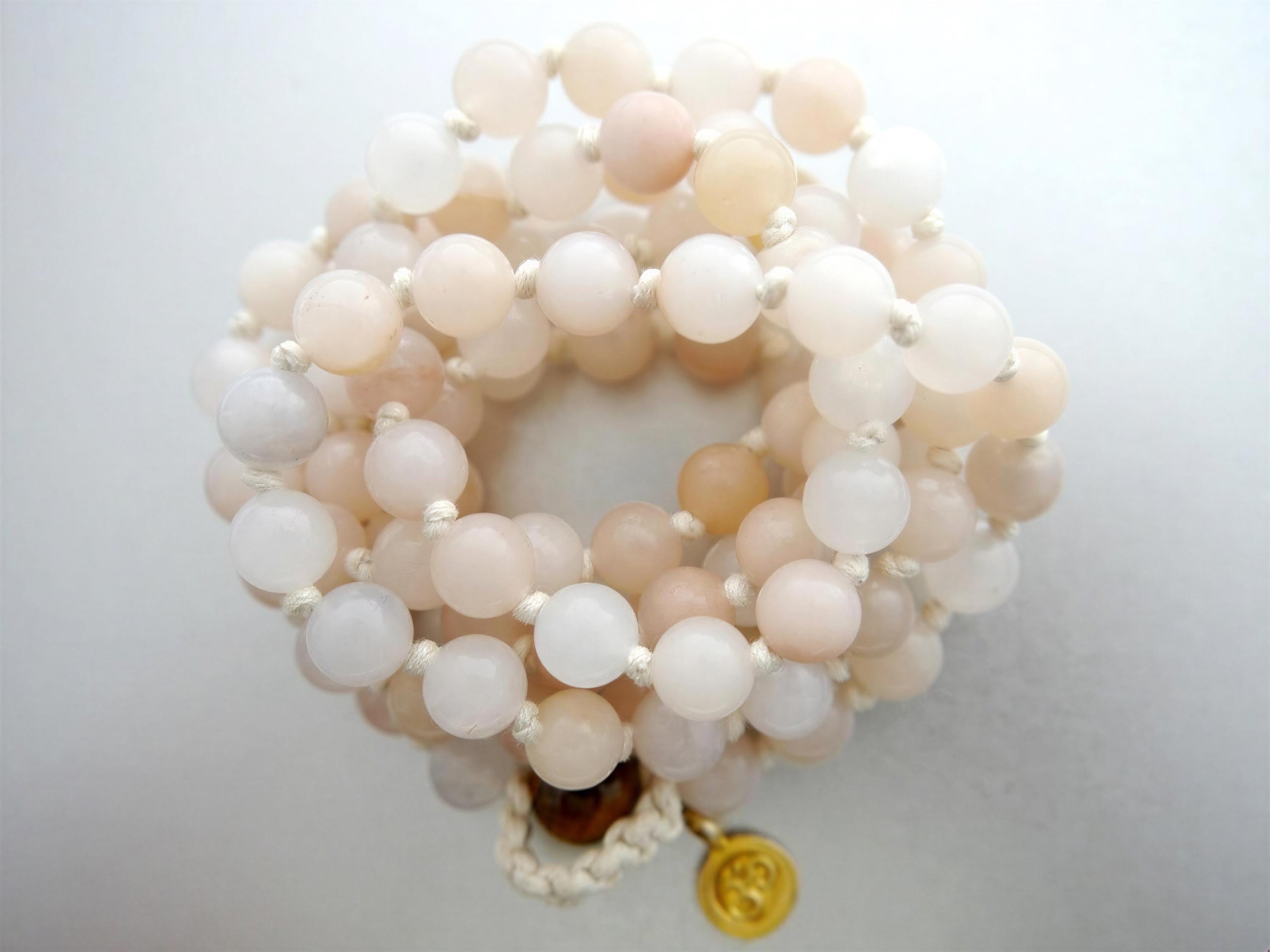A beaded bracelet with a gold charm, featuring a variety of light pink and white beads arranged in a circular pattern.