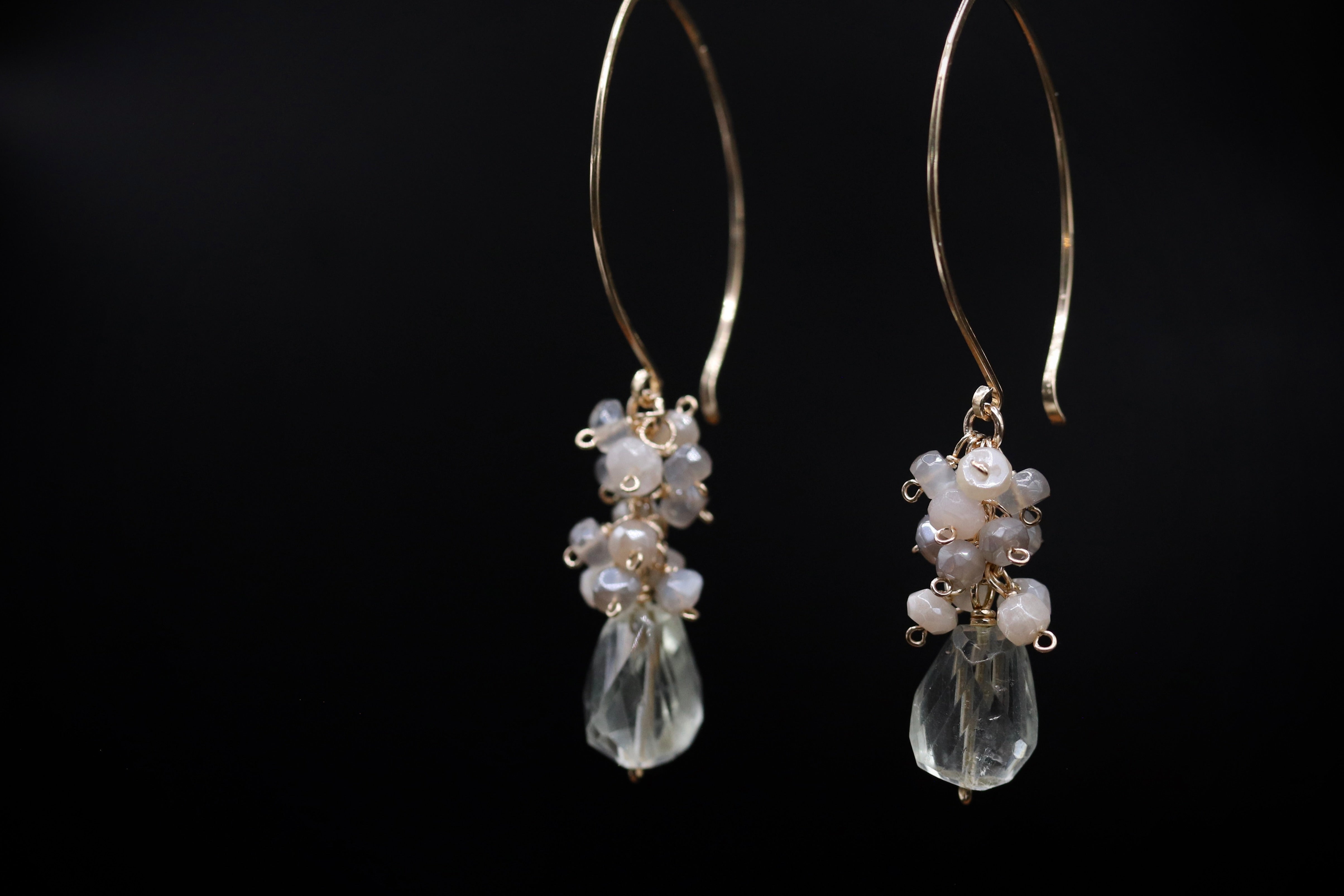 A pair of elegant earrings with clear gemstone pendants and metal hooks against a black background.