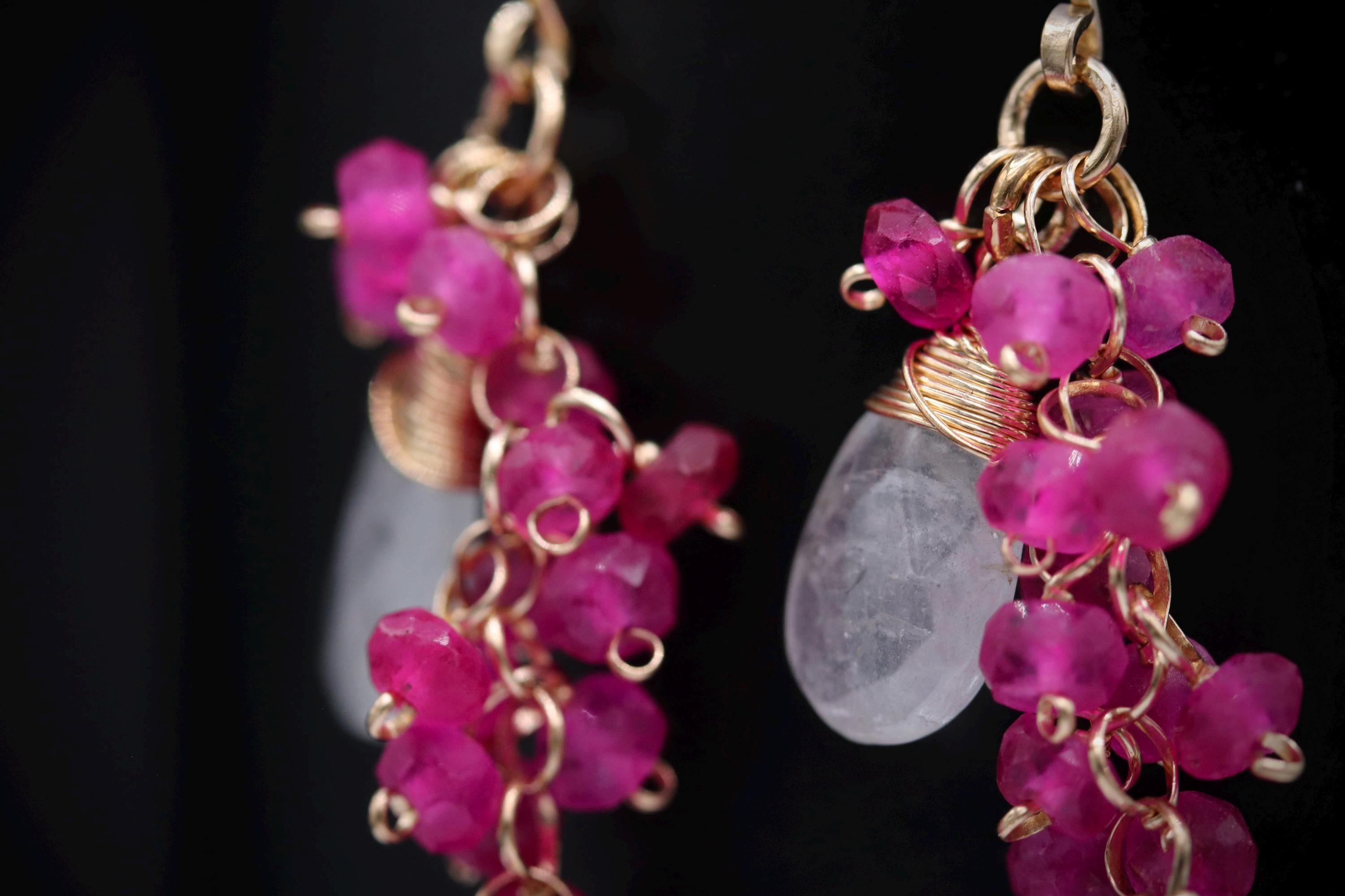 A close-up view of a pair of earrings with a combination of clear crystal and pink gemstone elements.