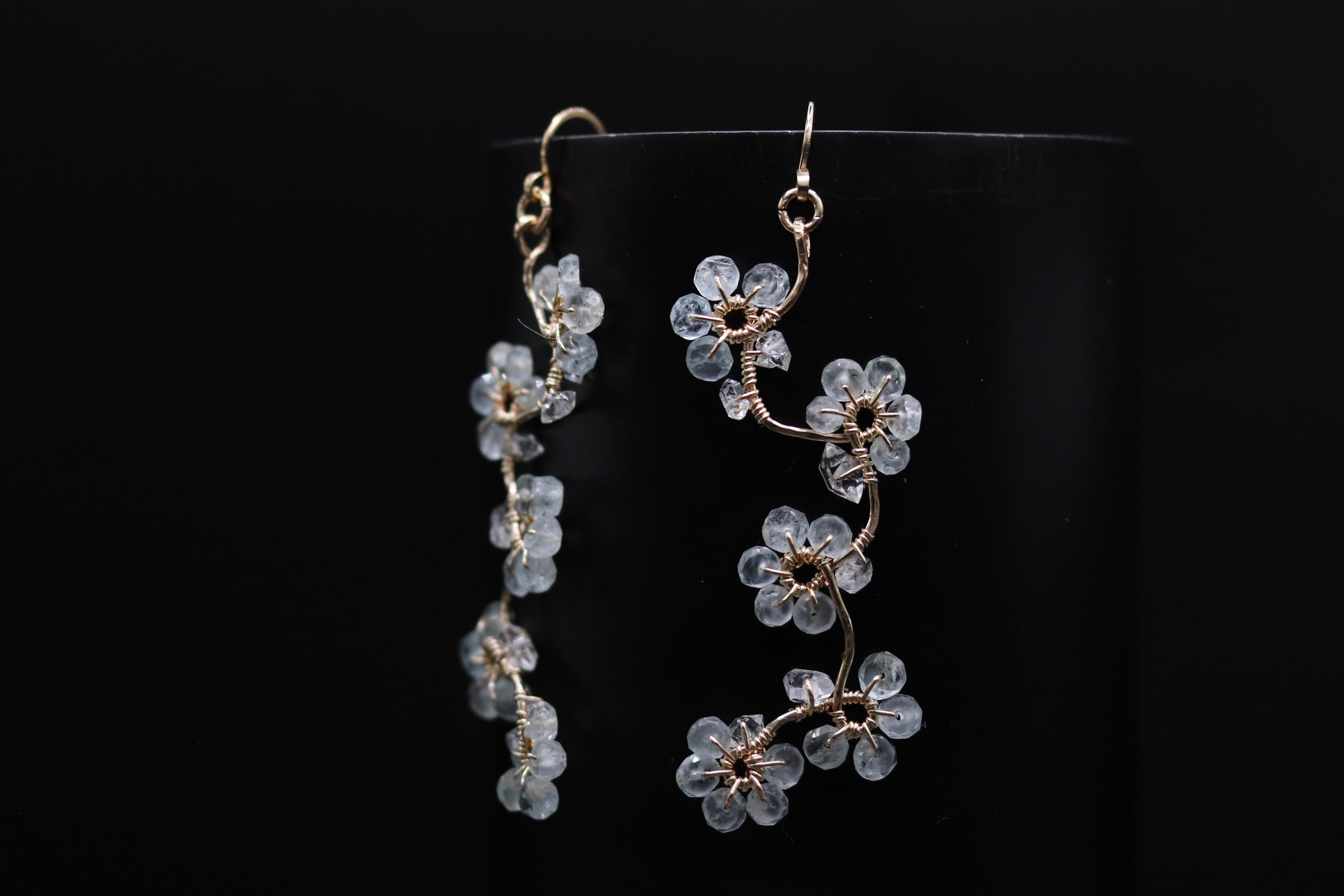 A pair of delicate earrings with clear crystal flowers on a black background.