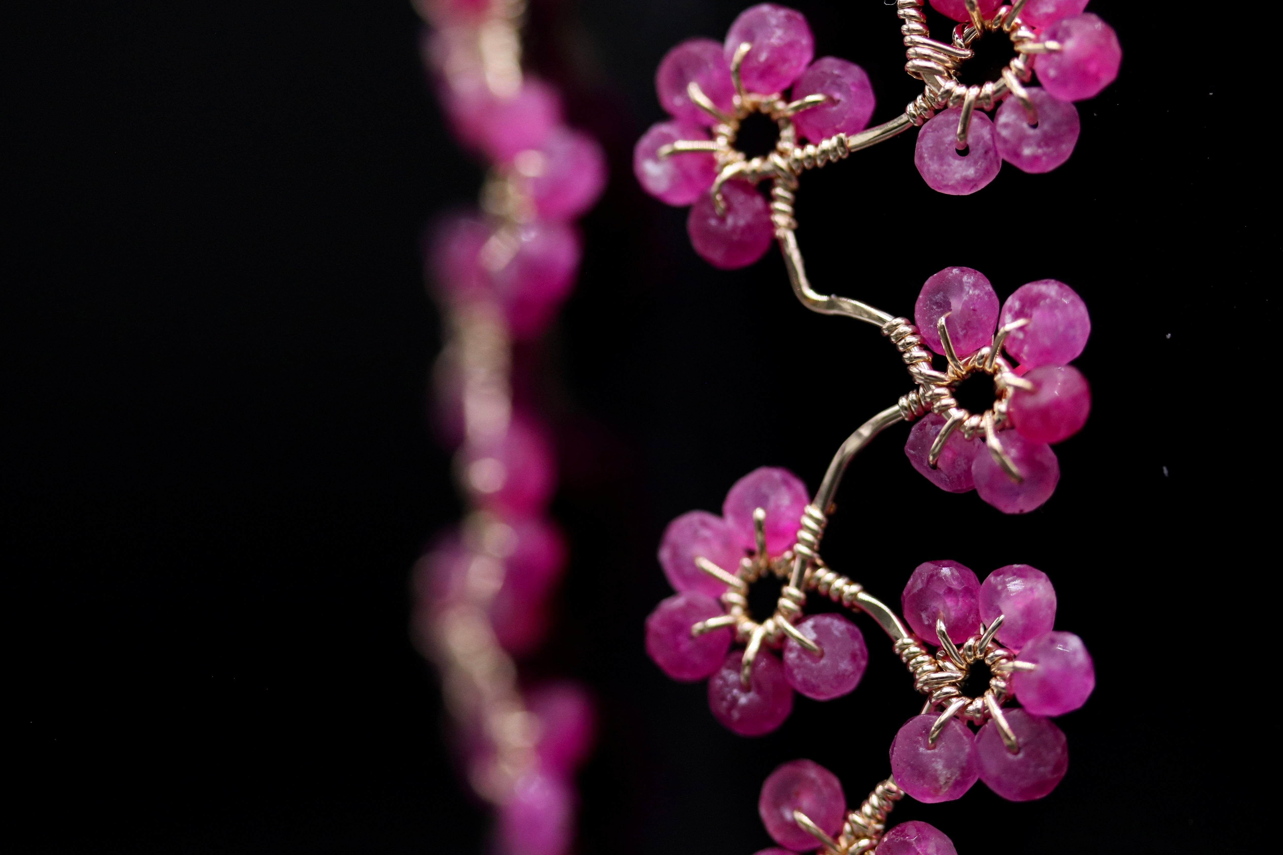 A close-up view of a delicate wire jewelry piece with small, round, pink gemstones arranged in a floral pattern.