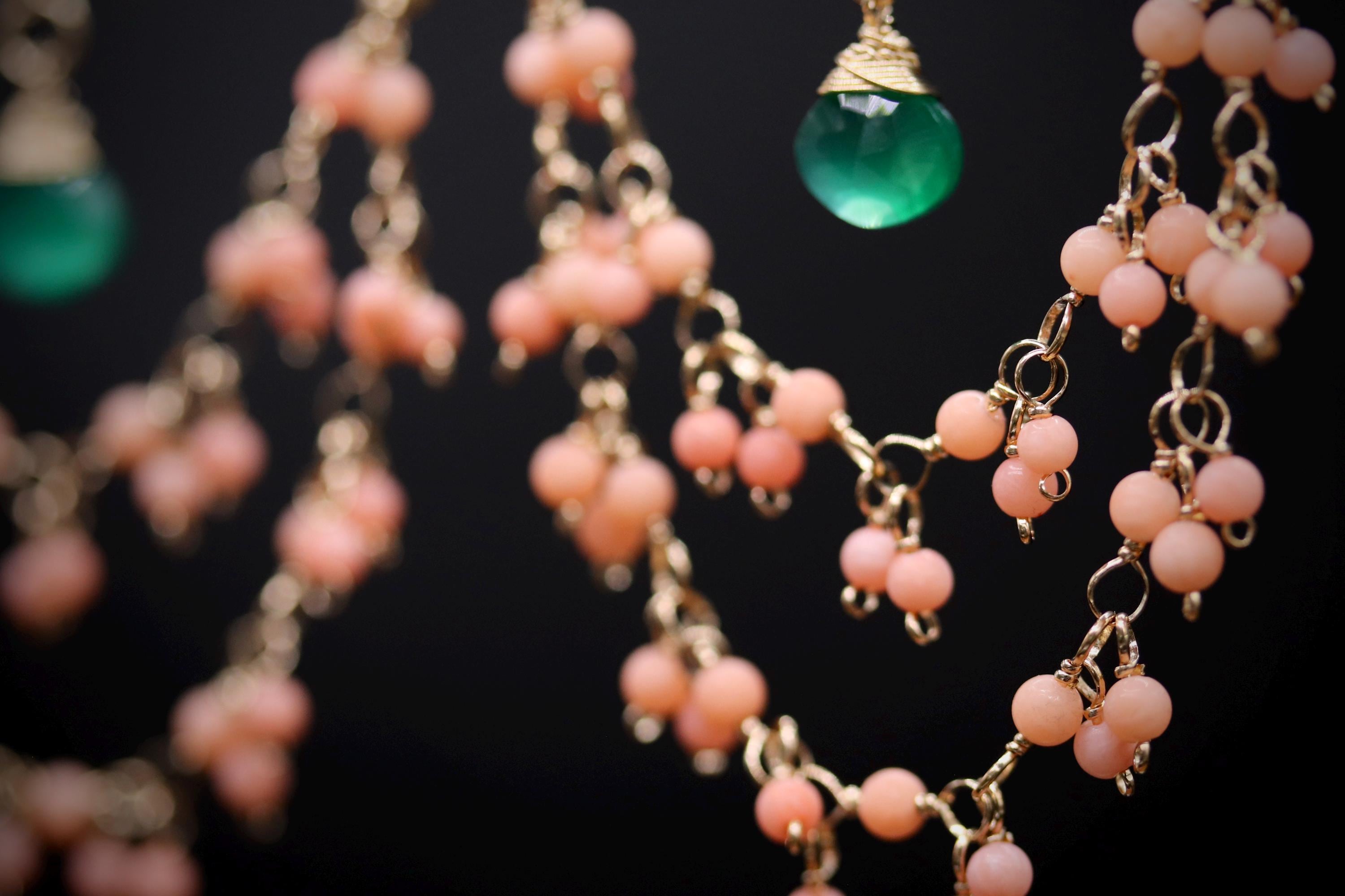 A close-up view of a necklace with a green glass bead and a cluster of pink beads.