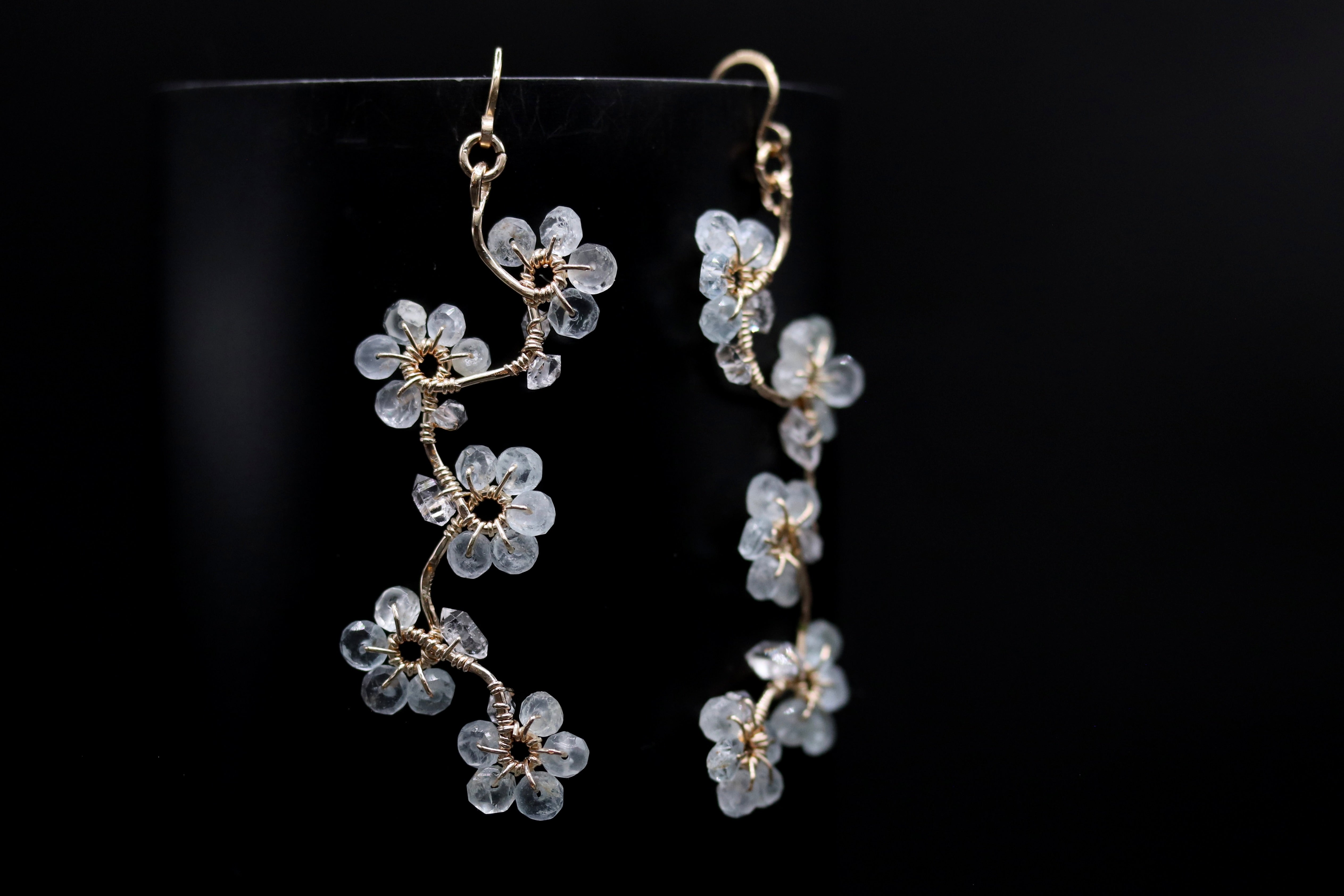 A pair of delicate earrings with clear flower-like designs, hanging against a black background.