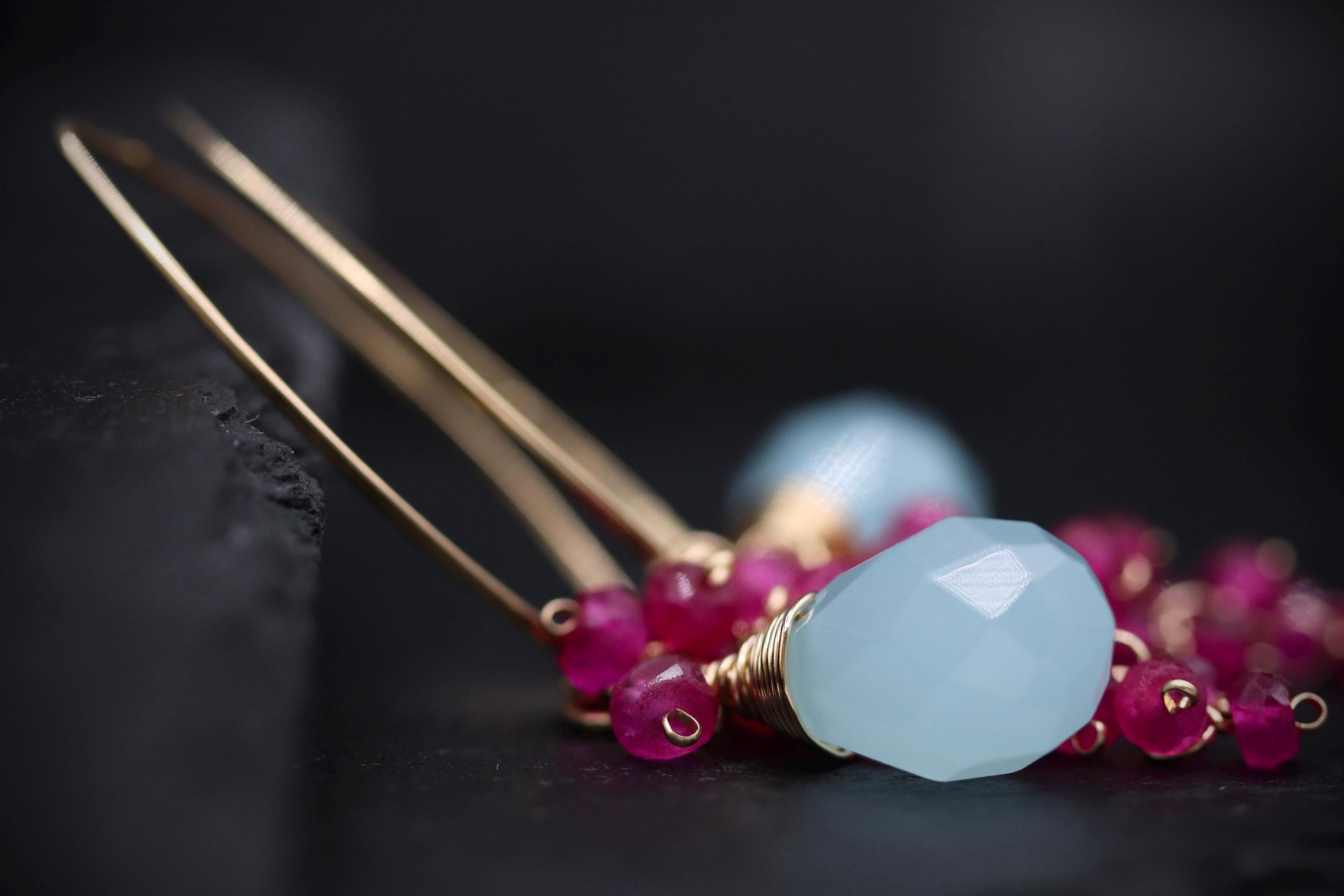 A close-up image of a pair of gold earrings with a large blue gemstone and a cluster of small pink gemstones.