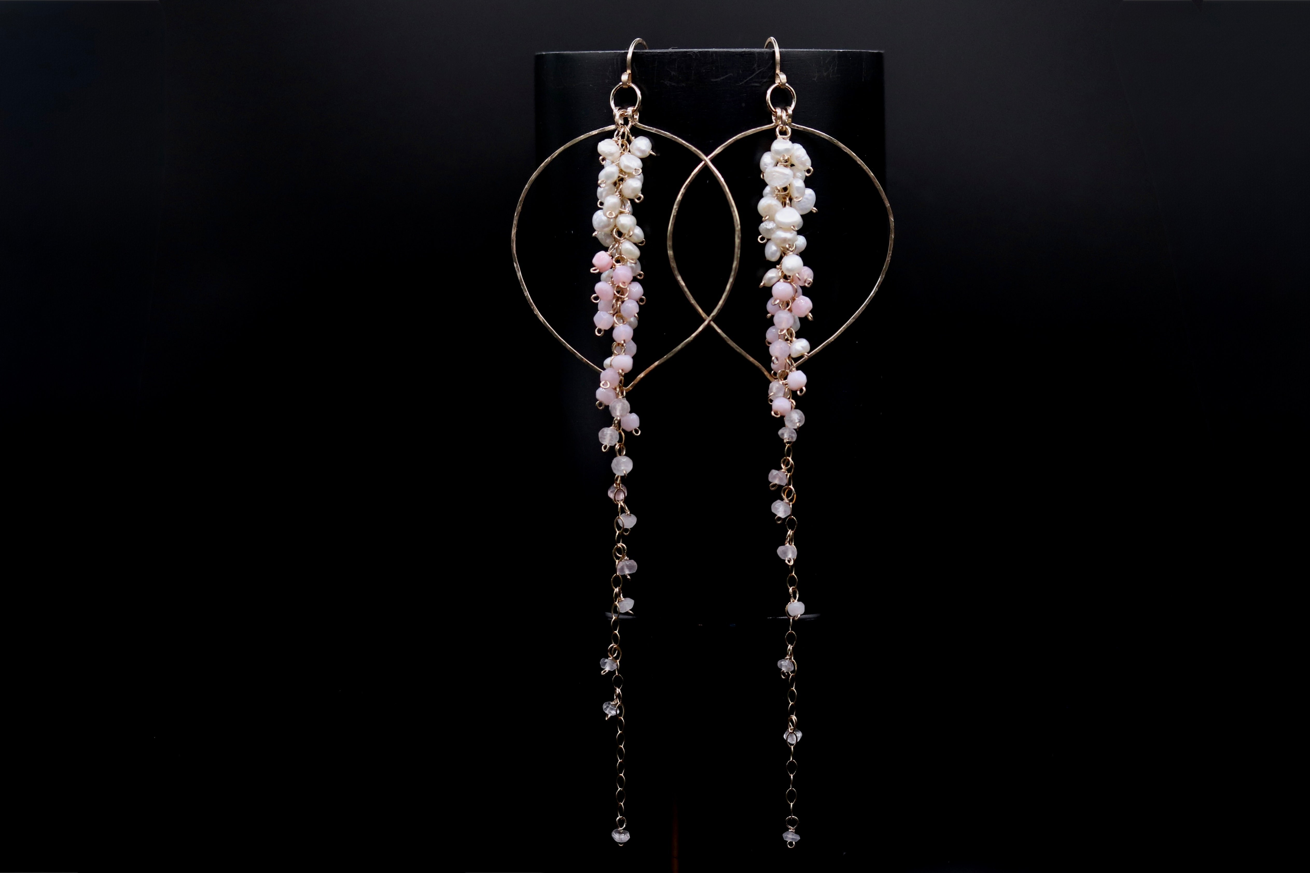 A pair of elegant earrings with long, dangling chains and small, white beads hanging from them, displayed against a black background.