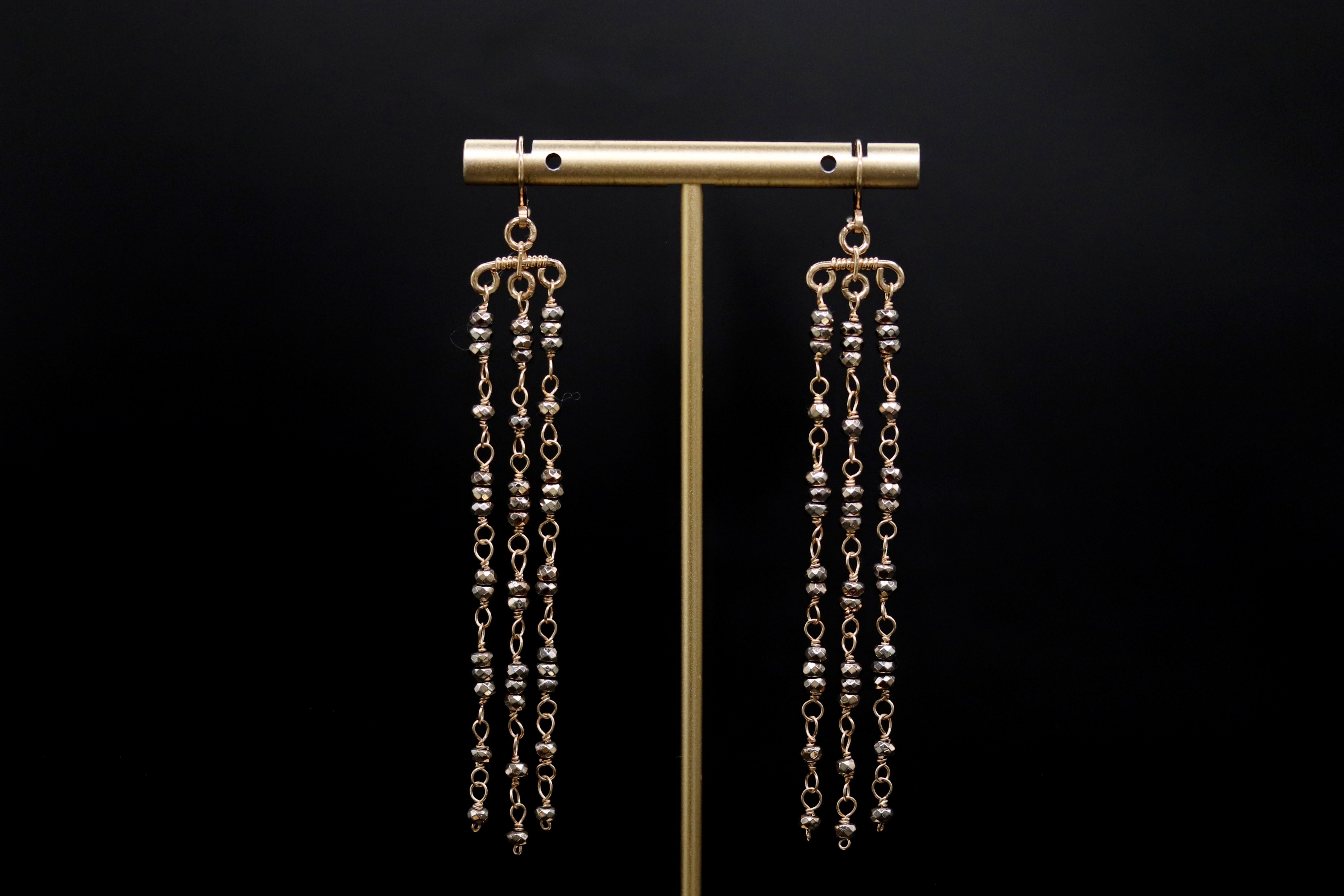 A pair of gold earrings with long, dangling chains hanging from the ear hooks against a black background.
