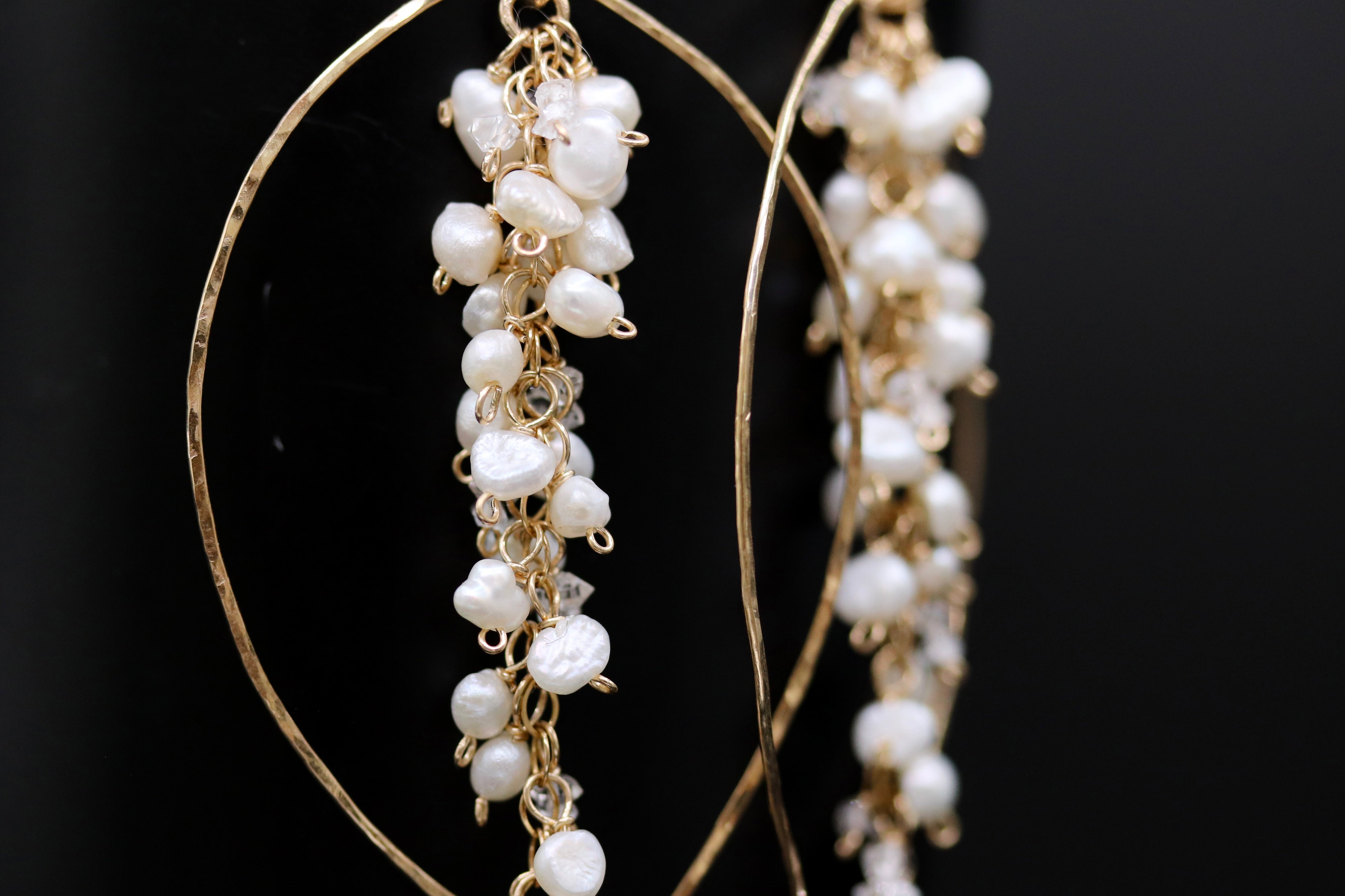 A close-up view of a pair of gold hoop earrings adorned with white pearls and dangling from a gold chain.