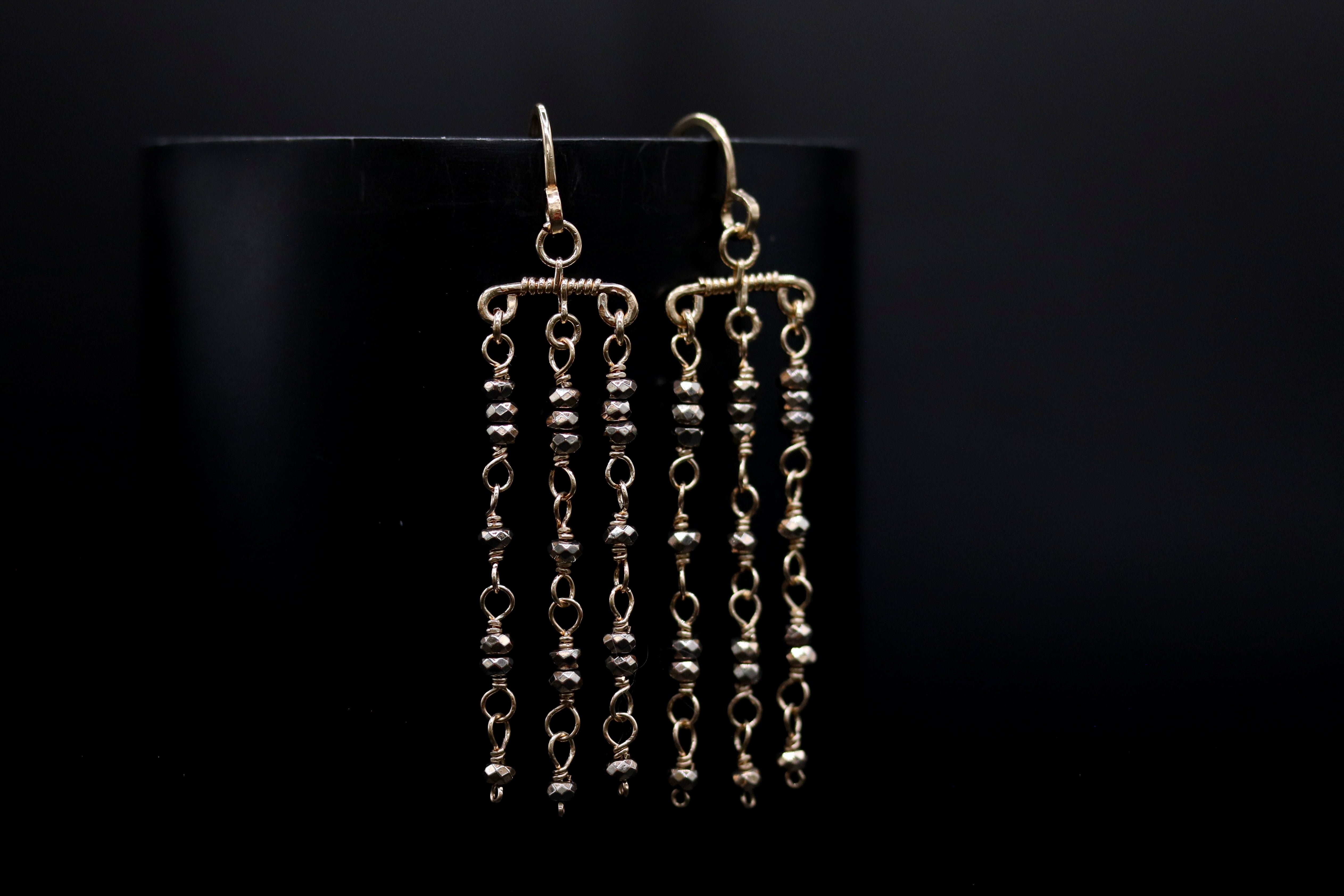 A pair of gold earrings with dangling beads, displayed against a black background.