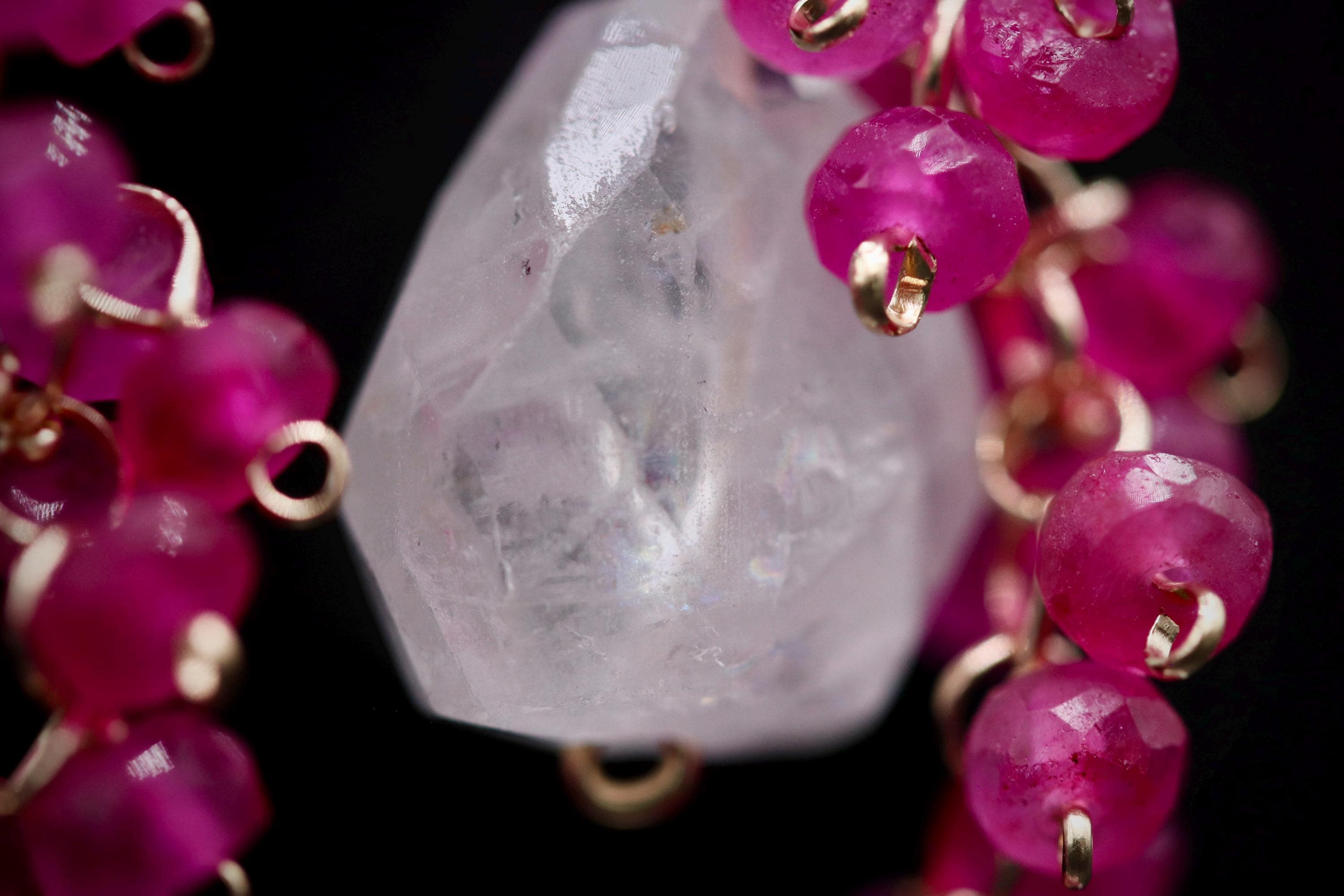 A close-up image of a crystal bead surrounded by a cluster of small, round, pink gemstones.
