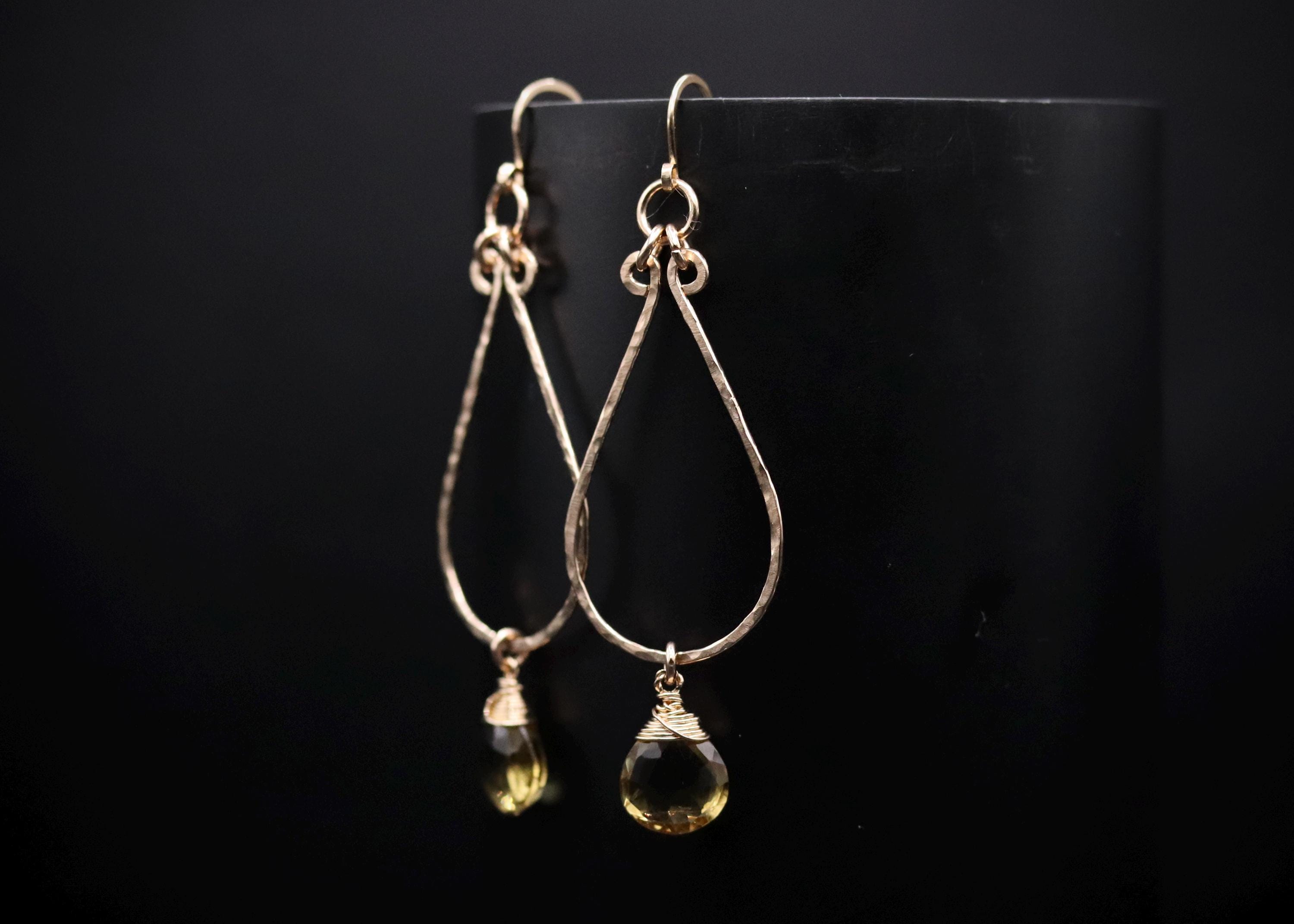A pair of gold earrings with a yellow gemstone hanging from them, displayed against a black background.