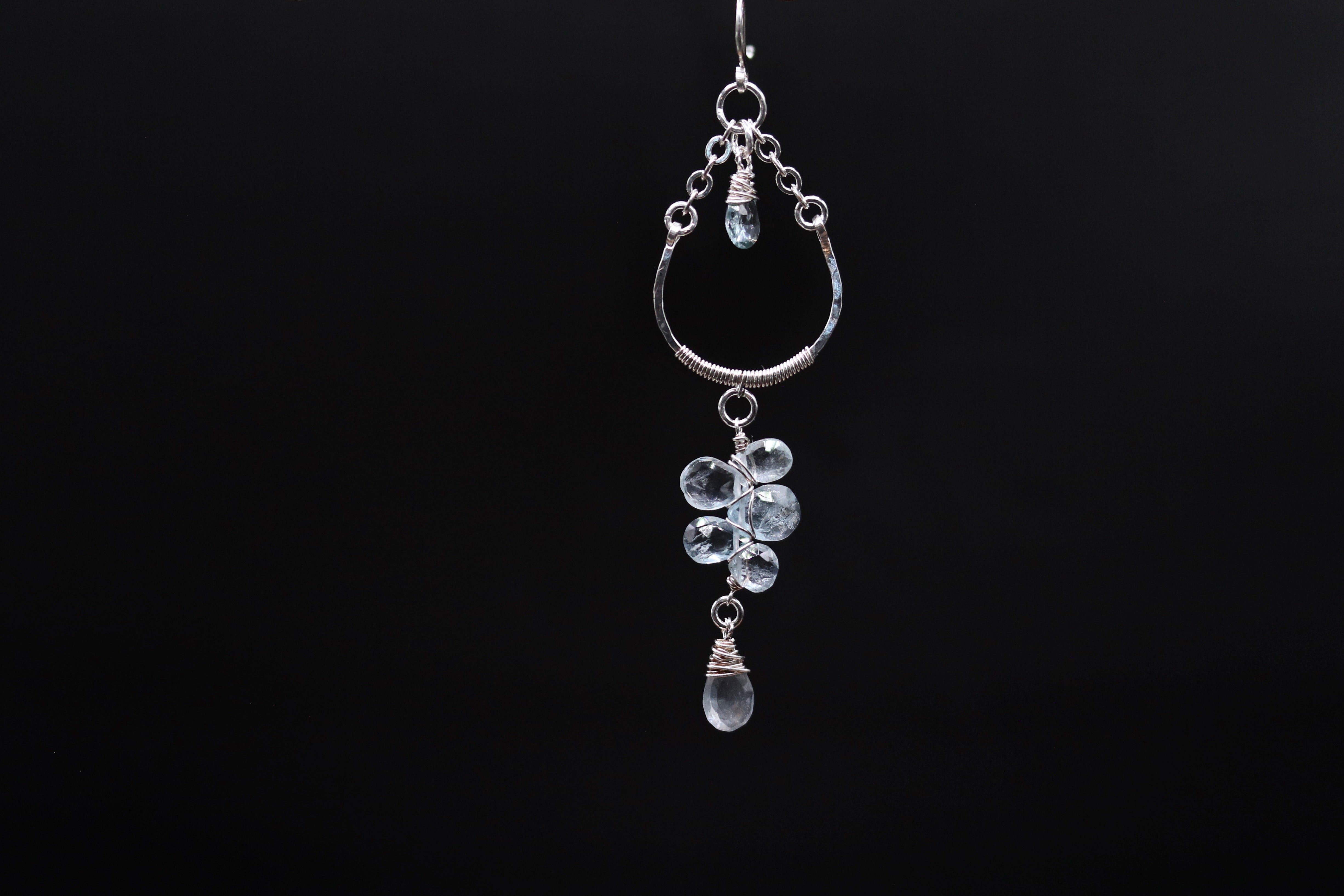 A silver earring with a clear gemstone dangling from it, suspended against a black background.