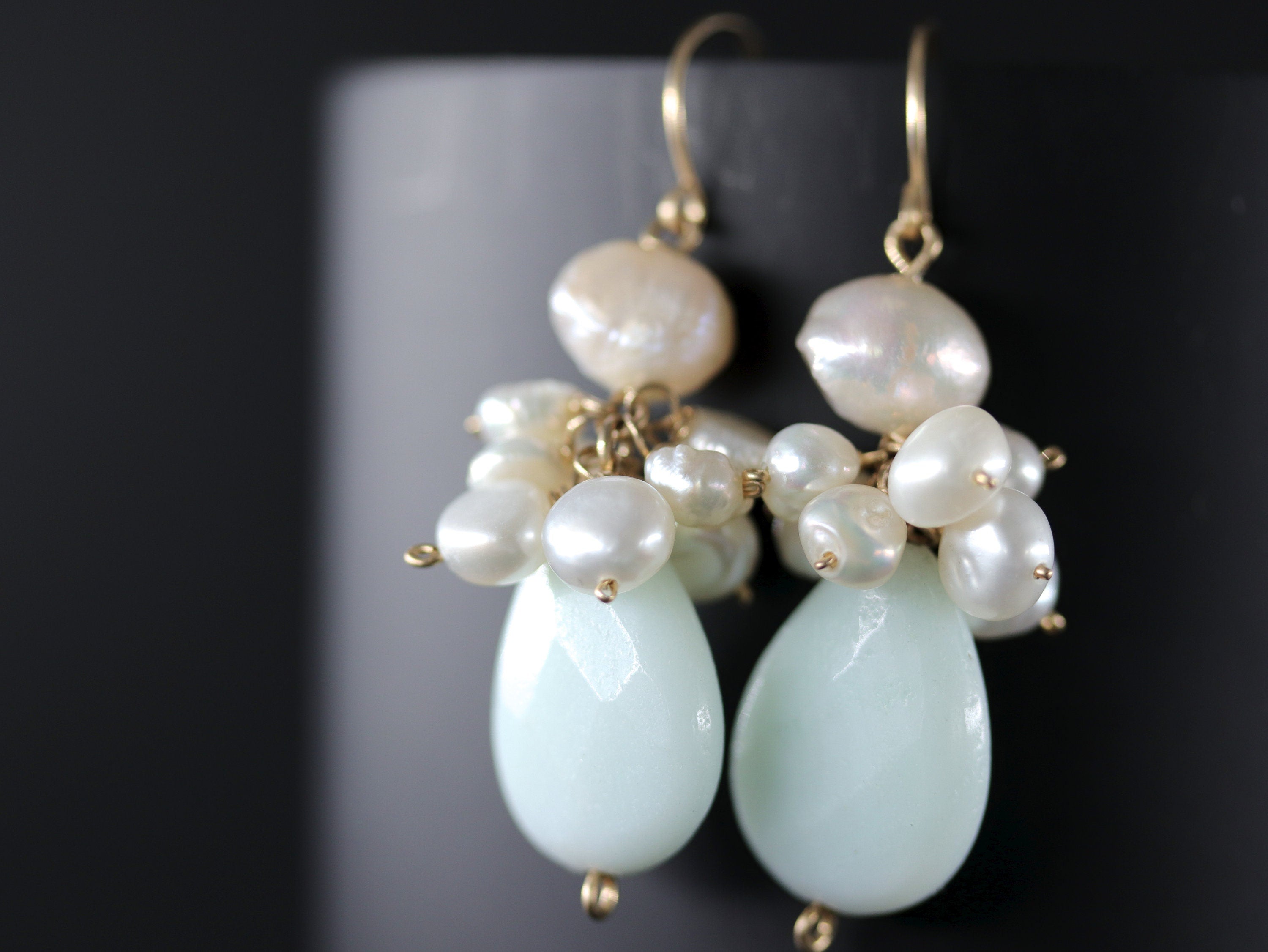May include: A pair of dangle earrings with a teardrop-shaped light blue stone and a cluster of white pearls.