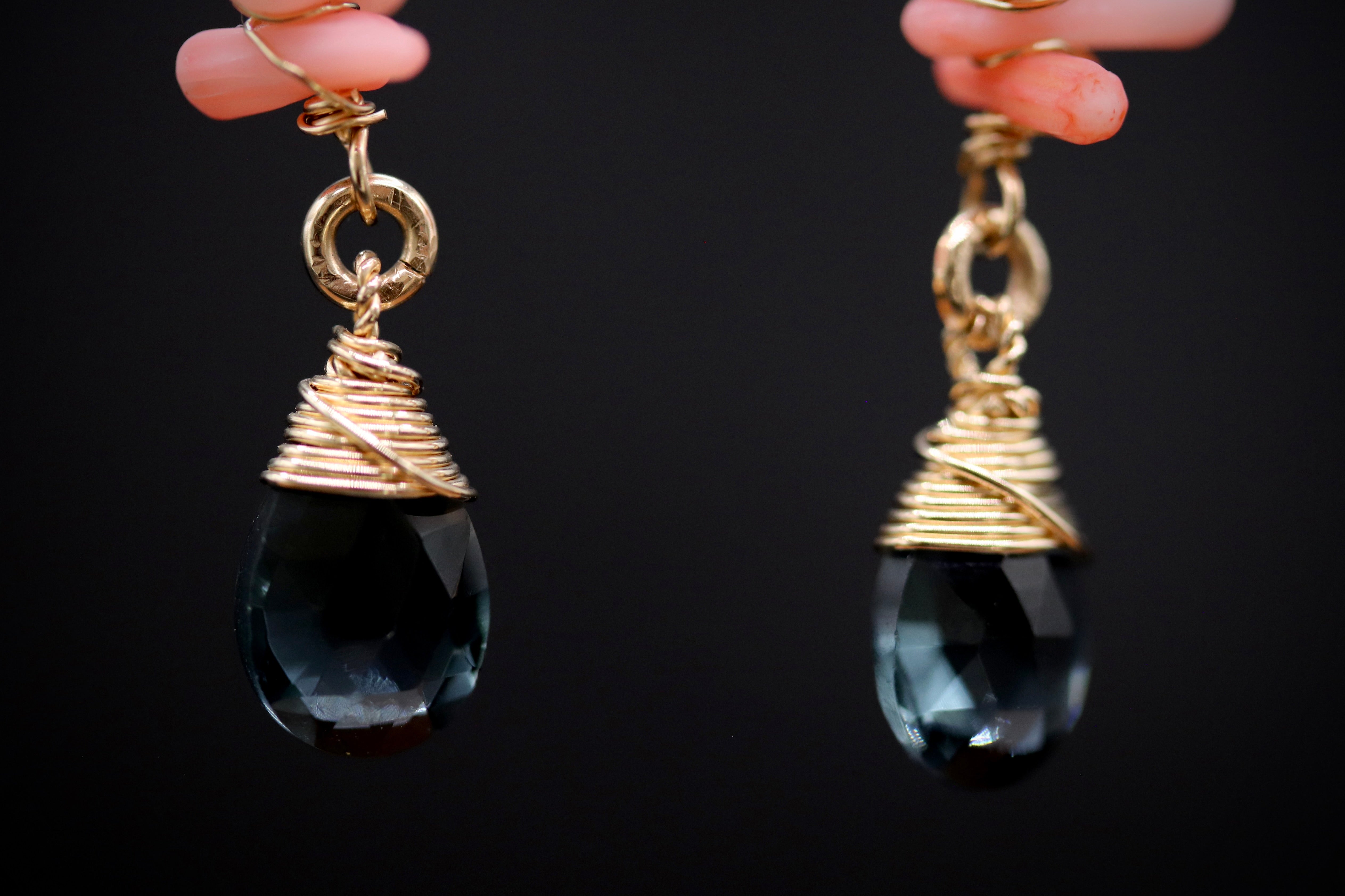 A pair of gold-colored earrings with black gemstone pendants, hanging against a dark background.