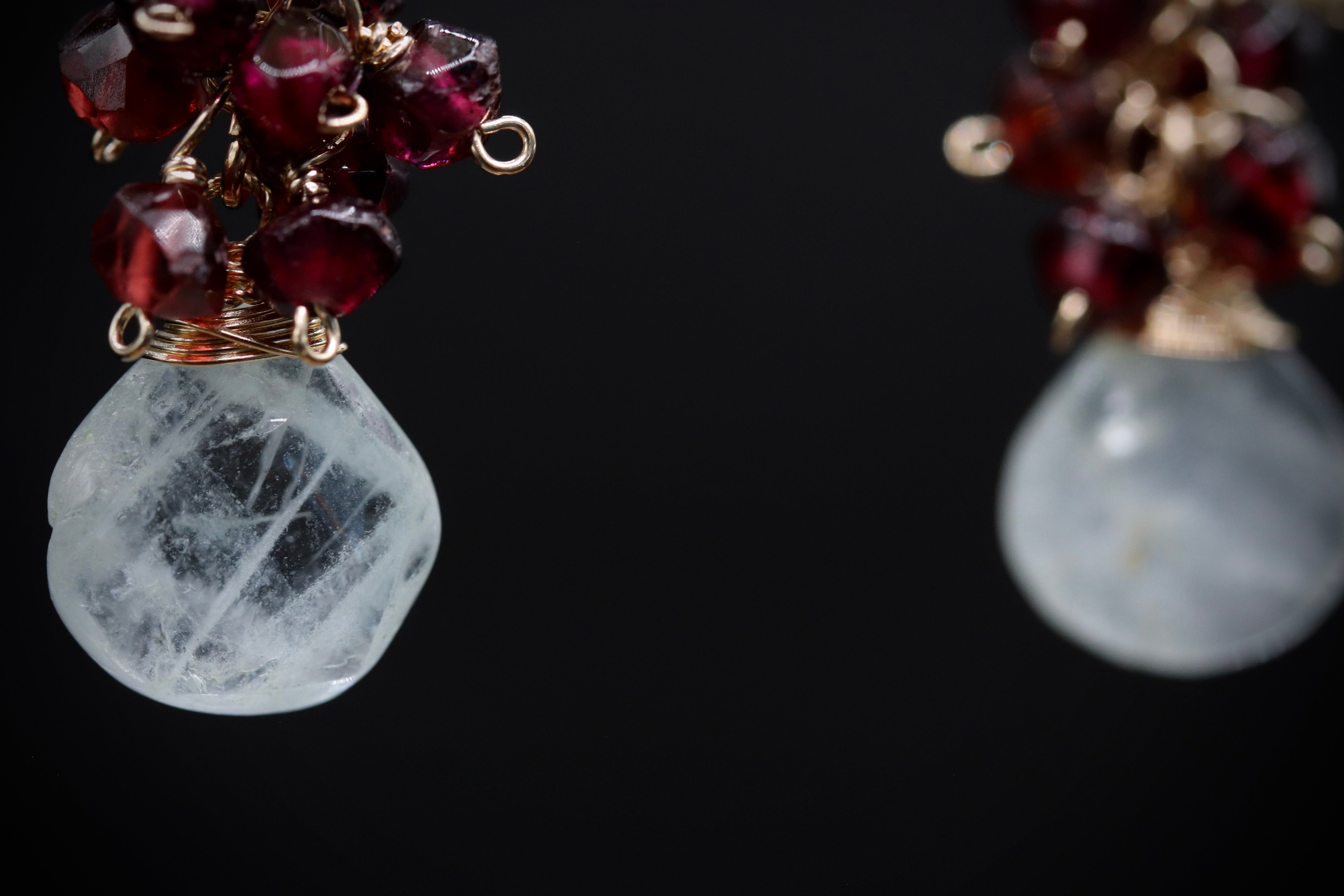 a pair of earrings with a clear crystal pendant and a cluster of red gemstones, such as garnets, attached to the crystal.