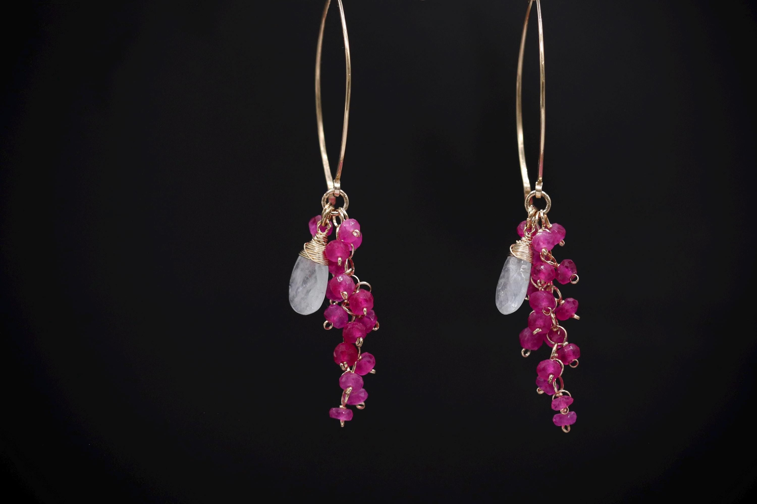 A pair of gold earrings with a long, dangling design and small, round, pink gemstones.