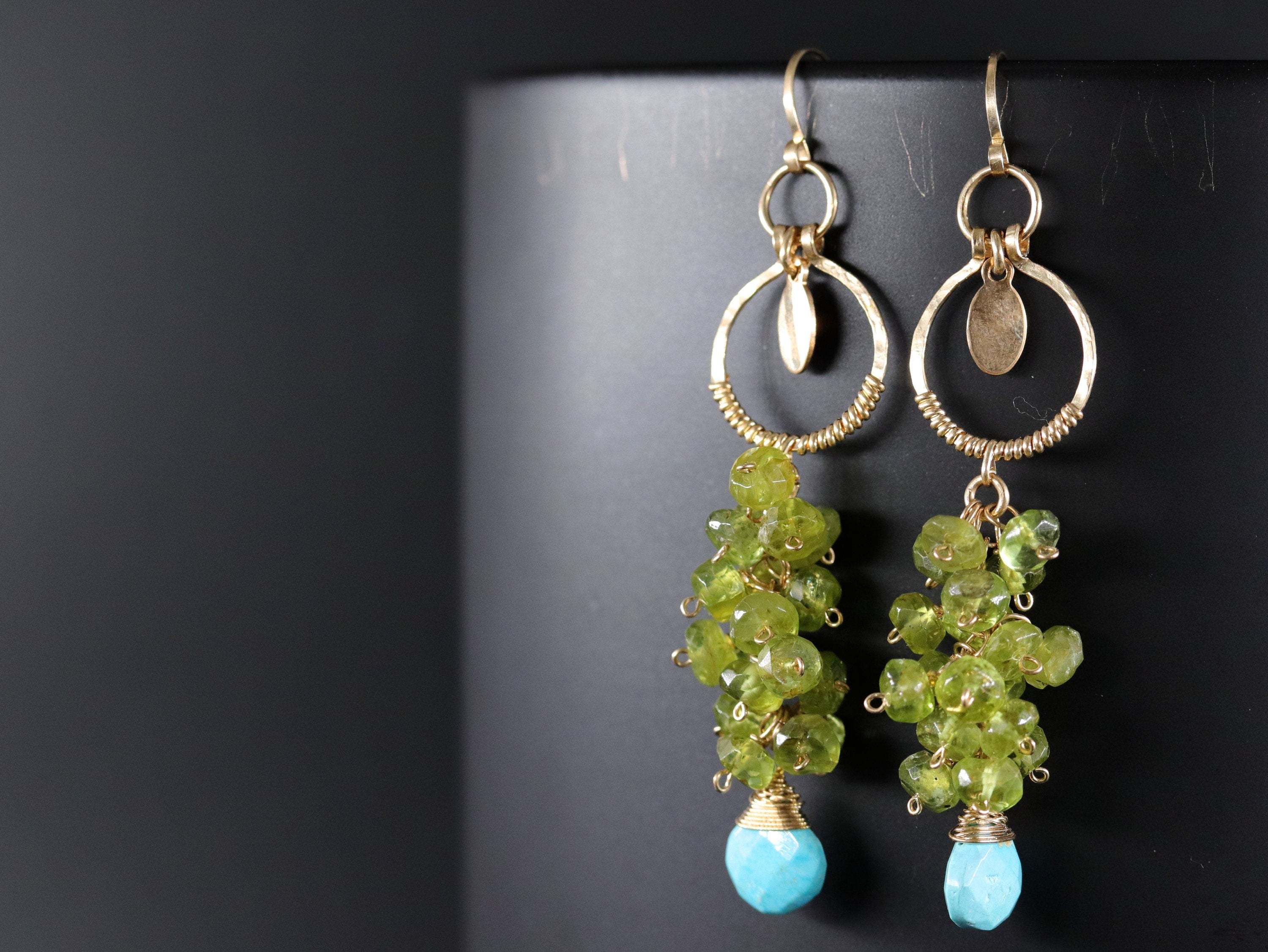 May include: Gold earrings with a delicate wire design and a cluster of green gemstones. The earrings feature a turquoise stone at the bottom.