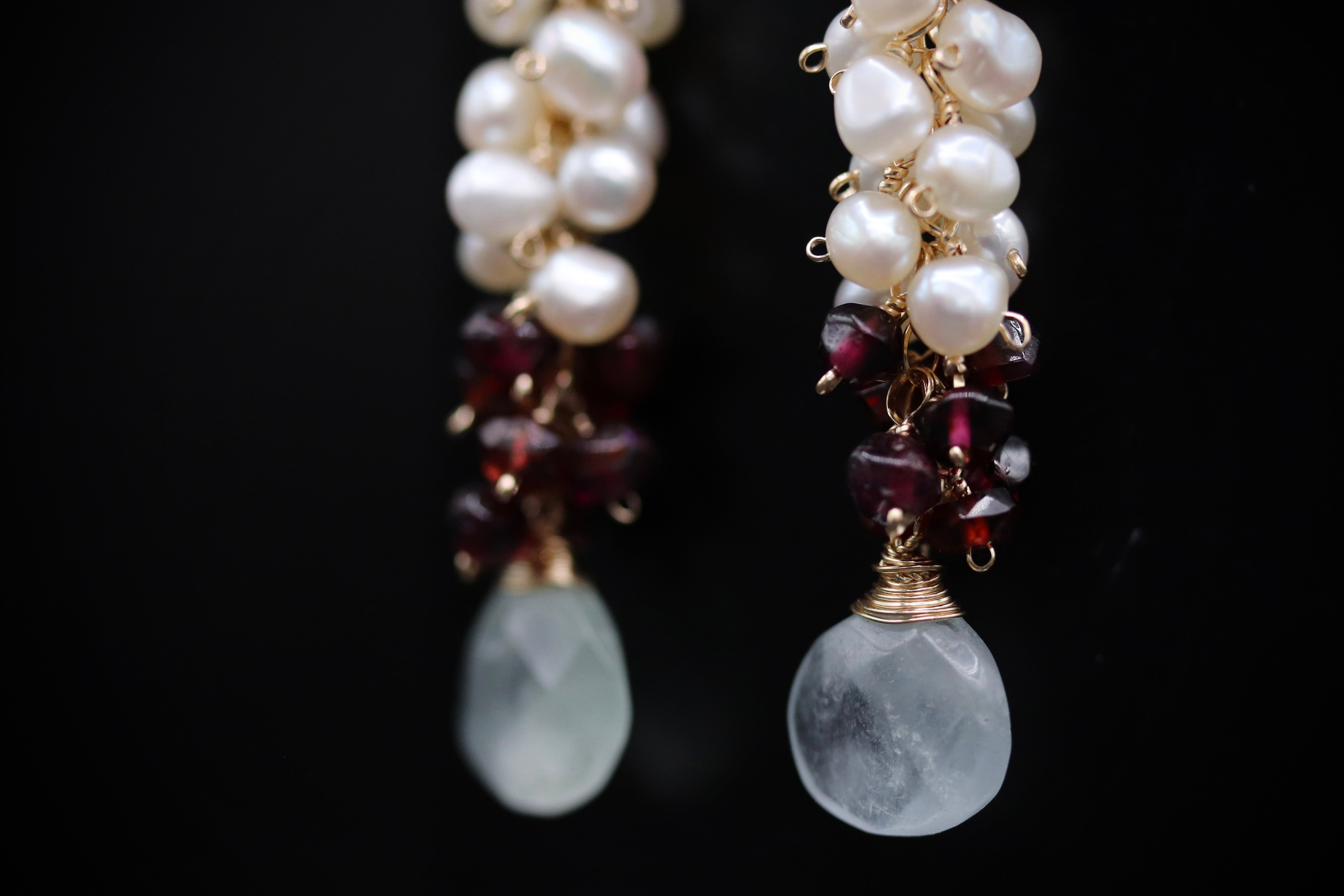 A pair of elegant earrings with white pearls and maroon gemstones hanging from a gold chain.