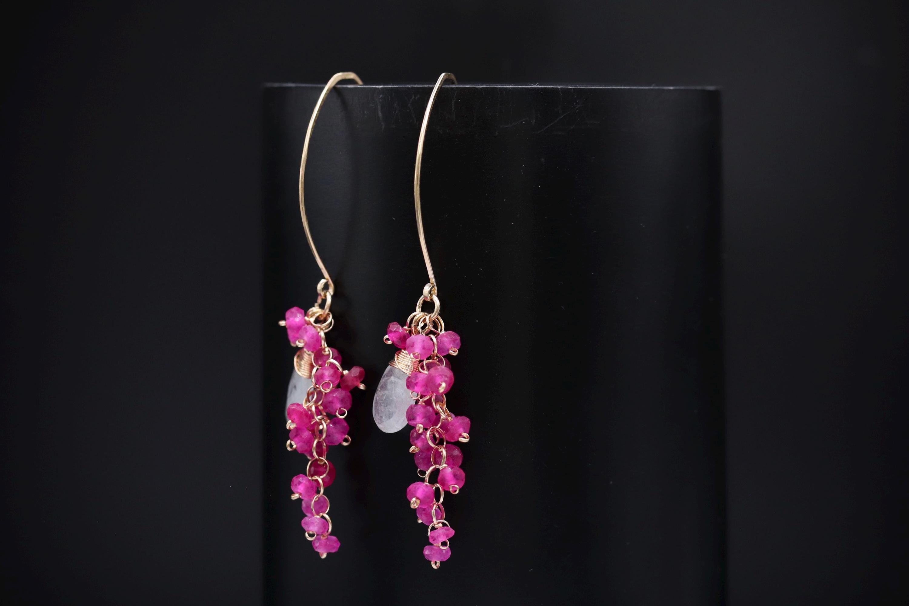 A pair of earrings with a long, dangling design and small, round, pink gemstones hanging from the bottom.