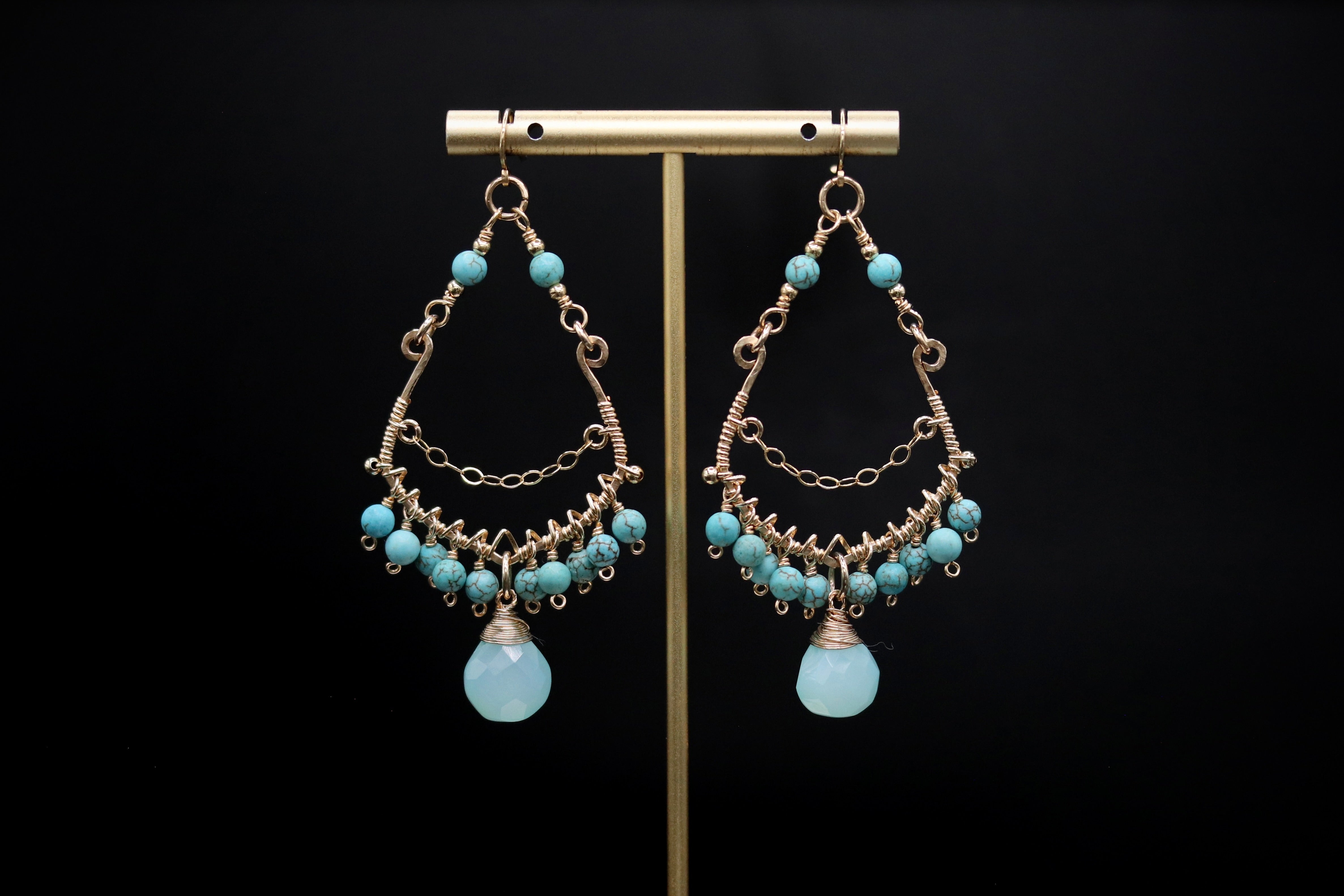 A pair of elegant earrings with turquoise stones and intricate metalwork, displayed on a gold stand against a black background.