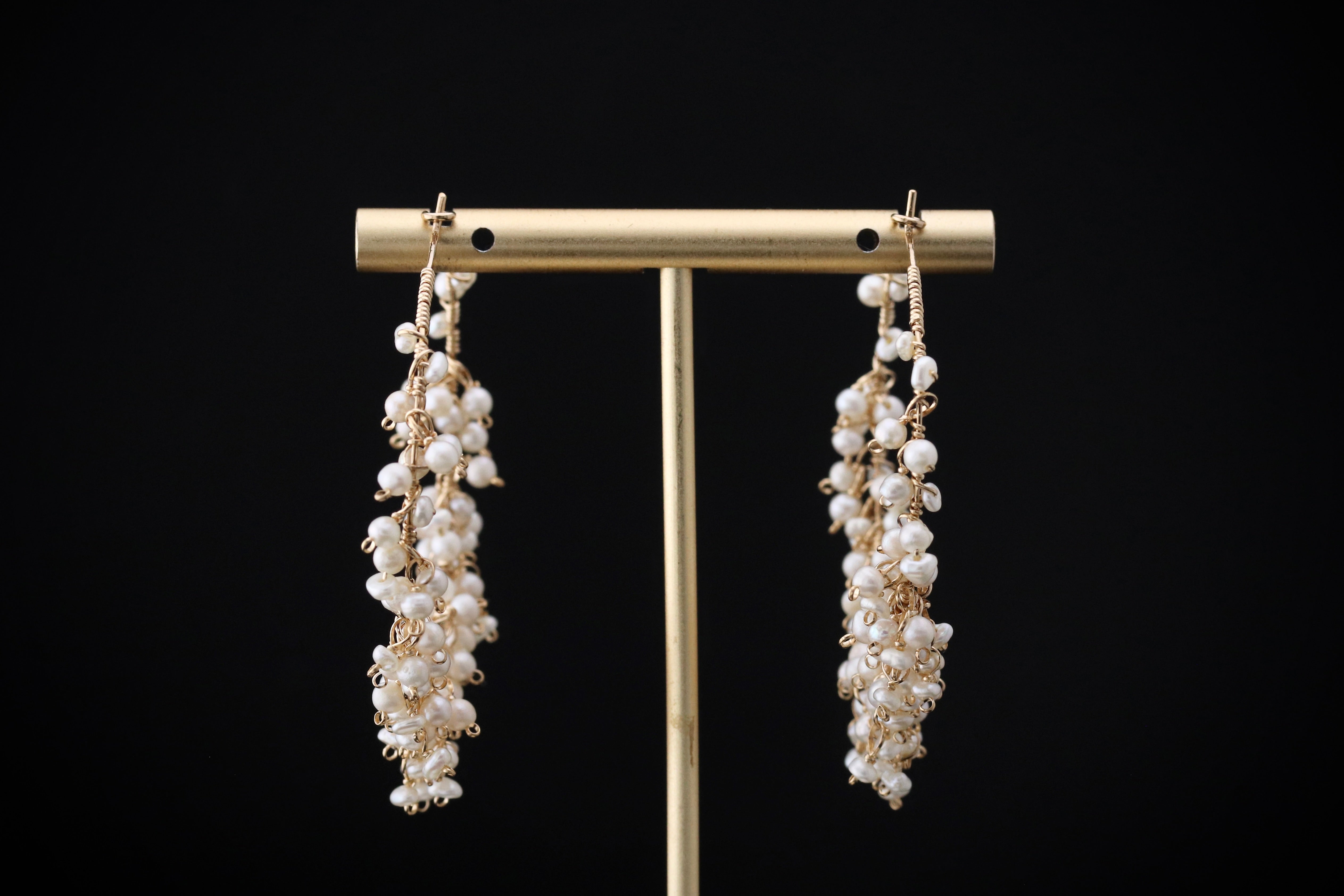 A pair of elegant earrings with white pearls hanging from a gold stand against a black background.