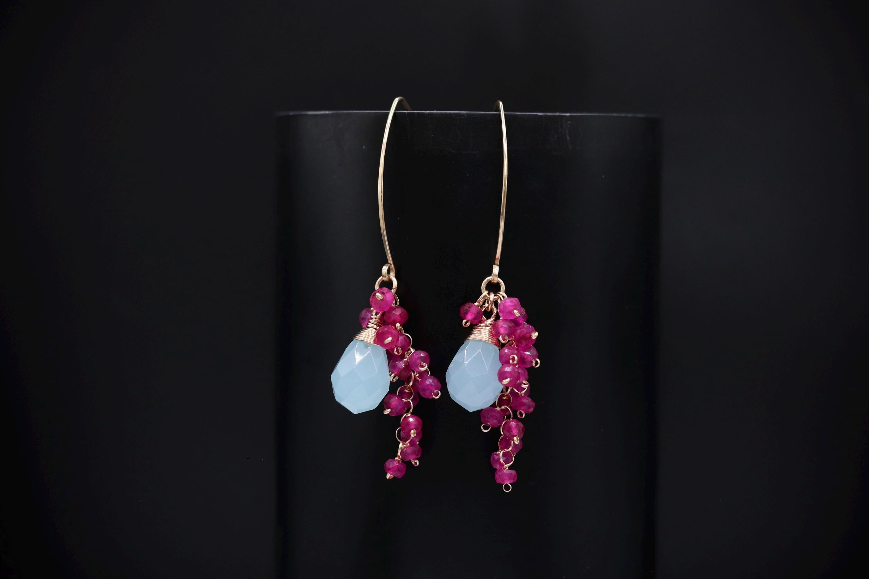 A pair of earrings with a combination of blue and pink gemstones, hanging from a gold hook.