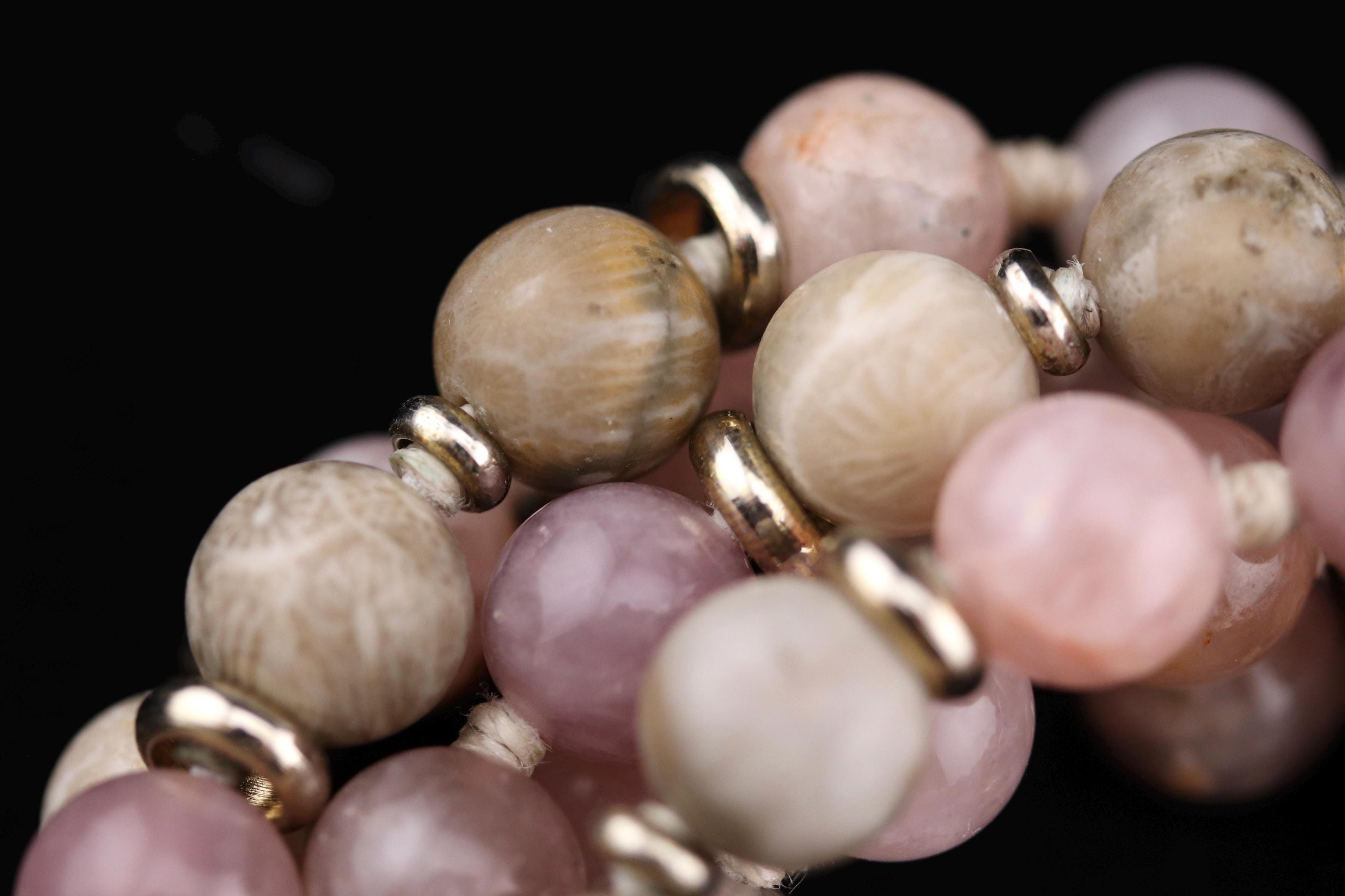 A close-up image of a collection of colorful beads, including coral and pink stones, arranged in a decorative manner.